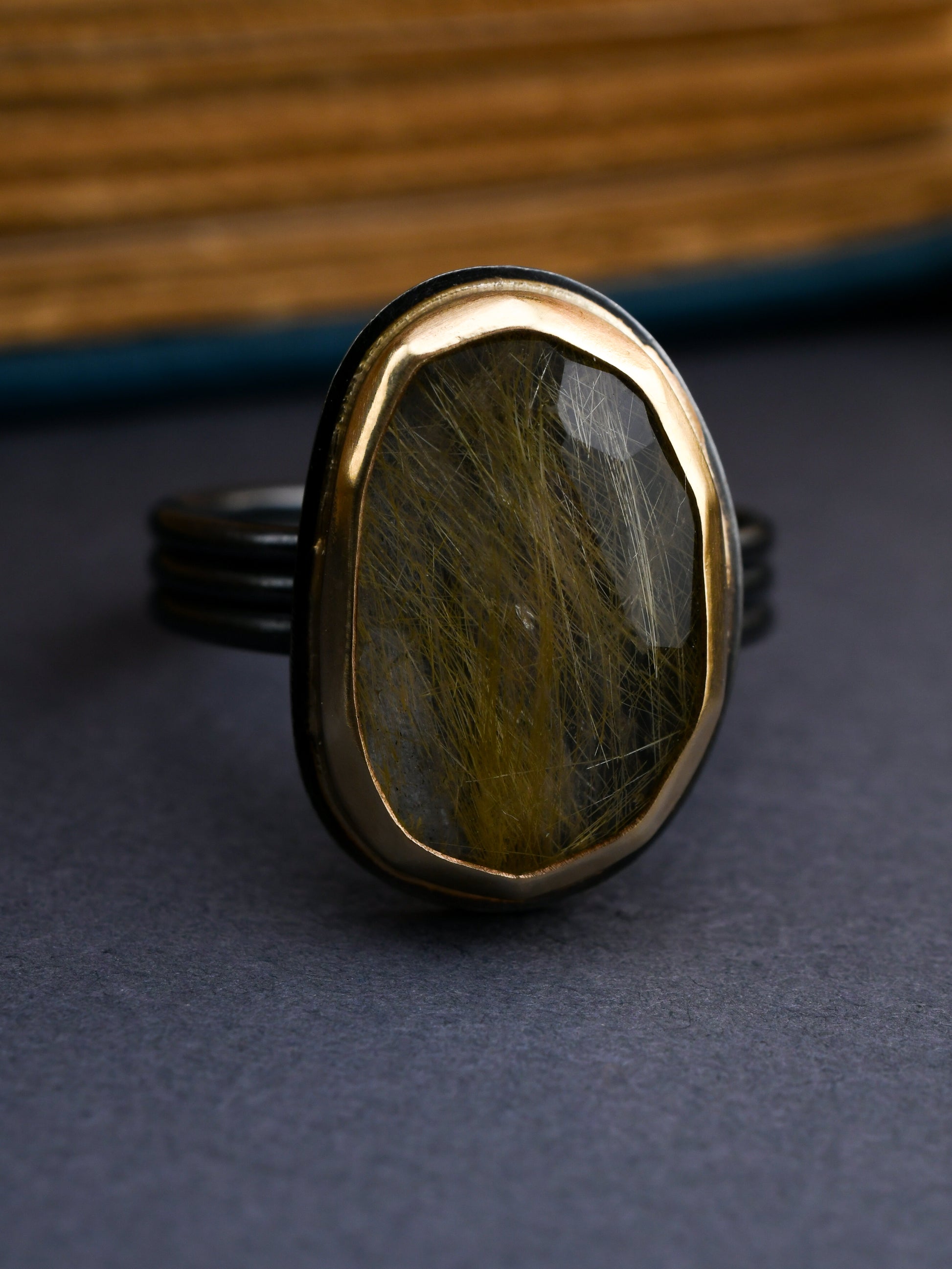 Black and gold ring with large rutilated quartz center stone on a dark background