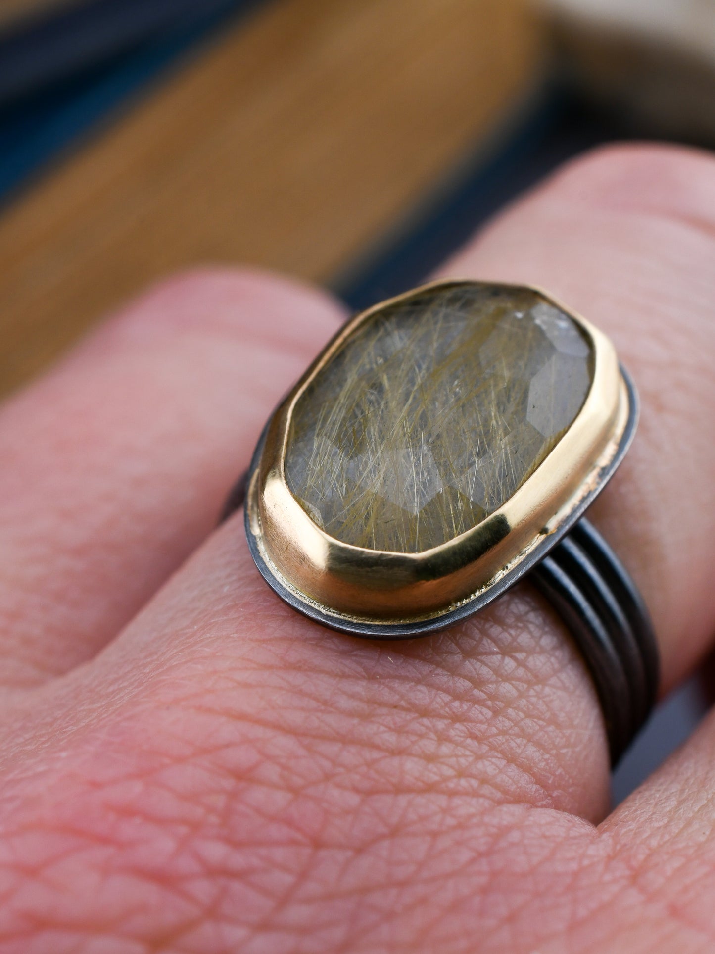 Black and gold rutilated quartz ring on a hand with a dark background