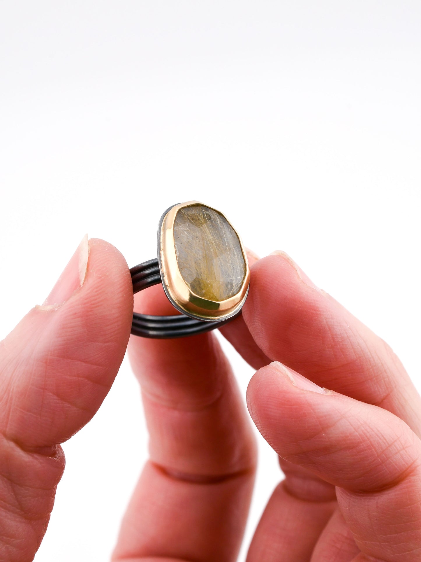 Black and gold rutilated quartz ring held in a hand on a white background