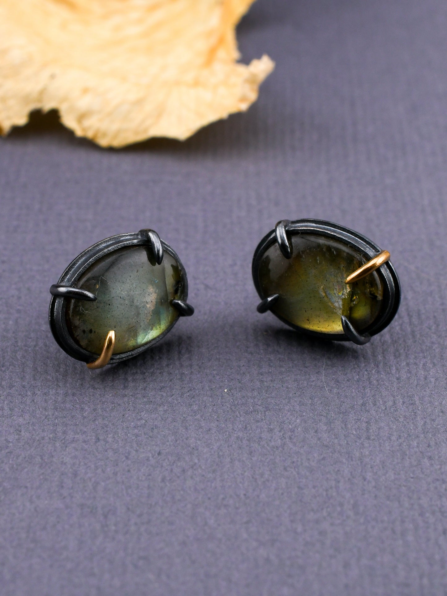 Pair of black-framed green stone earrings on a gray surface with a leaf in the background.