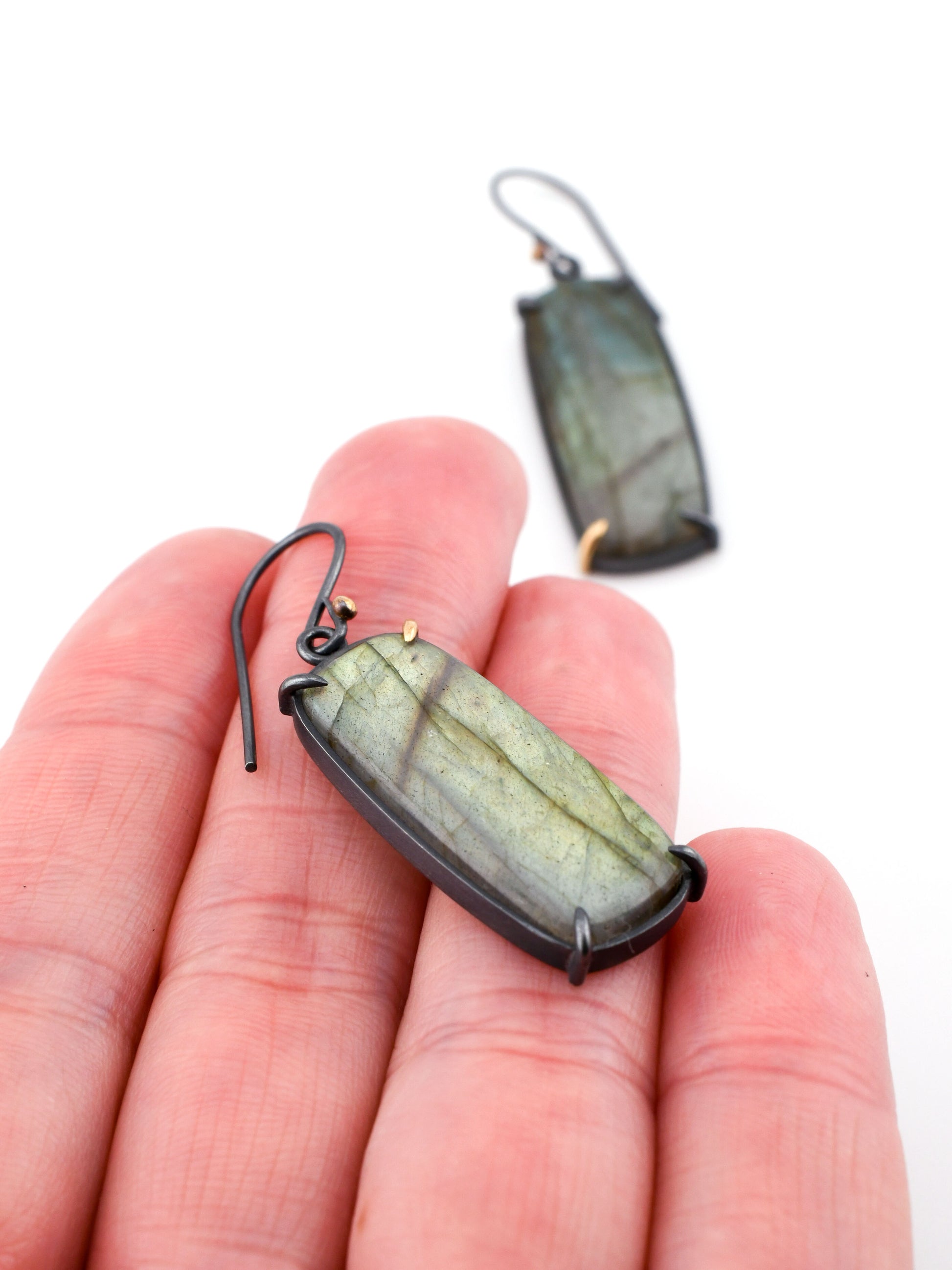 Labradorite earrings held in a hand with a white background