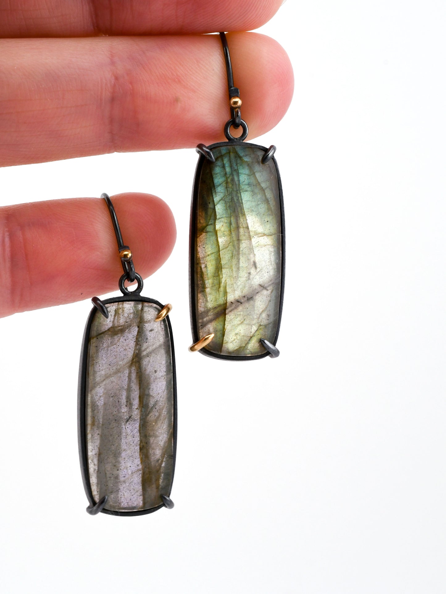 Labradorite earrings held between fingers against a white background