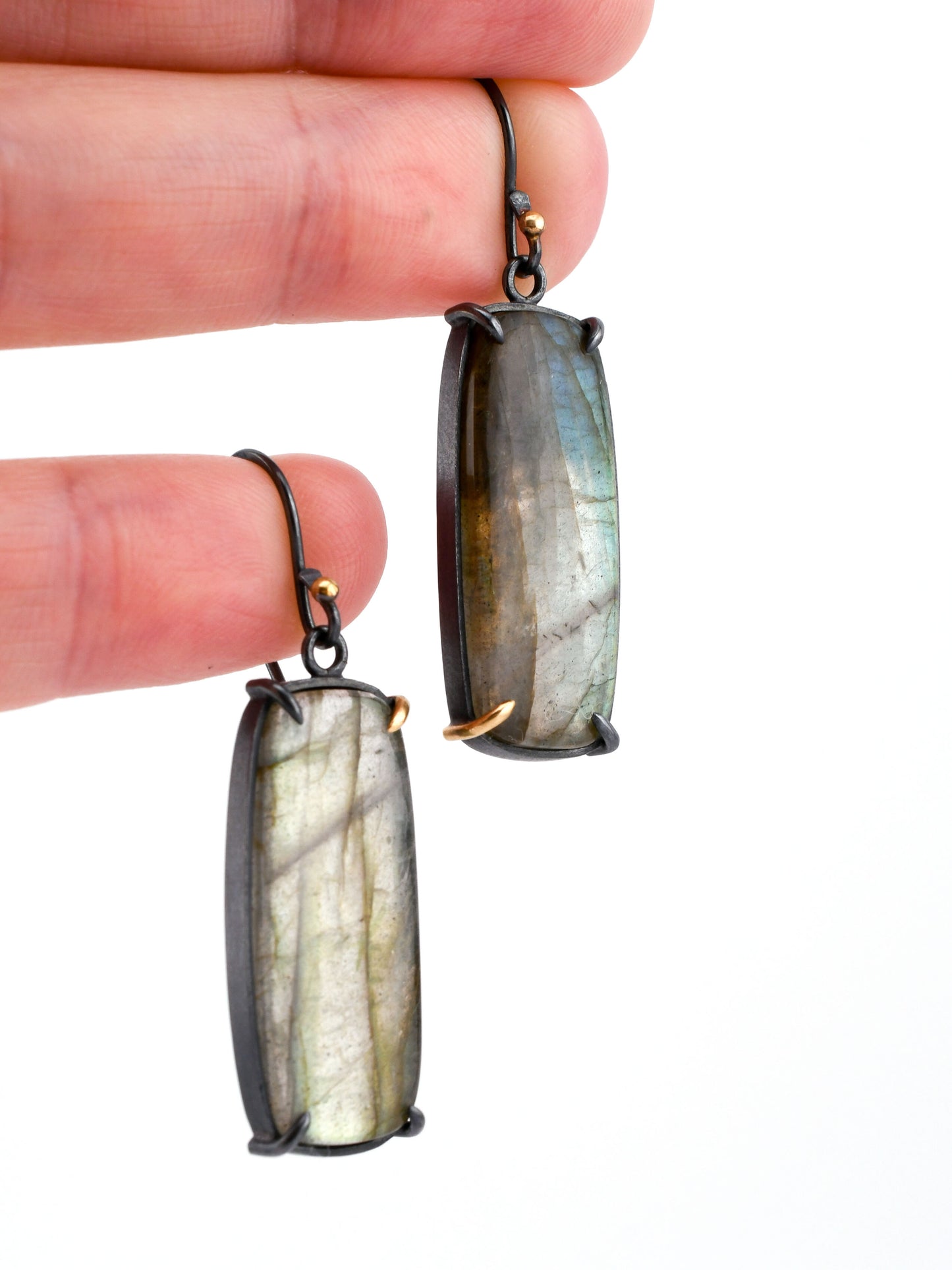 Labradorite earrings held between fingers against a white background