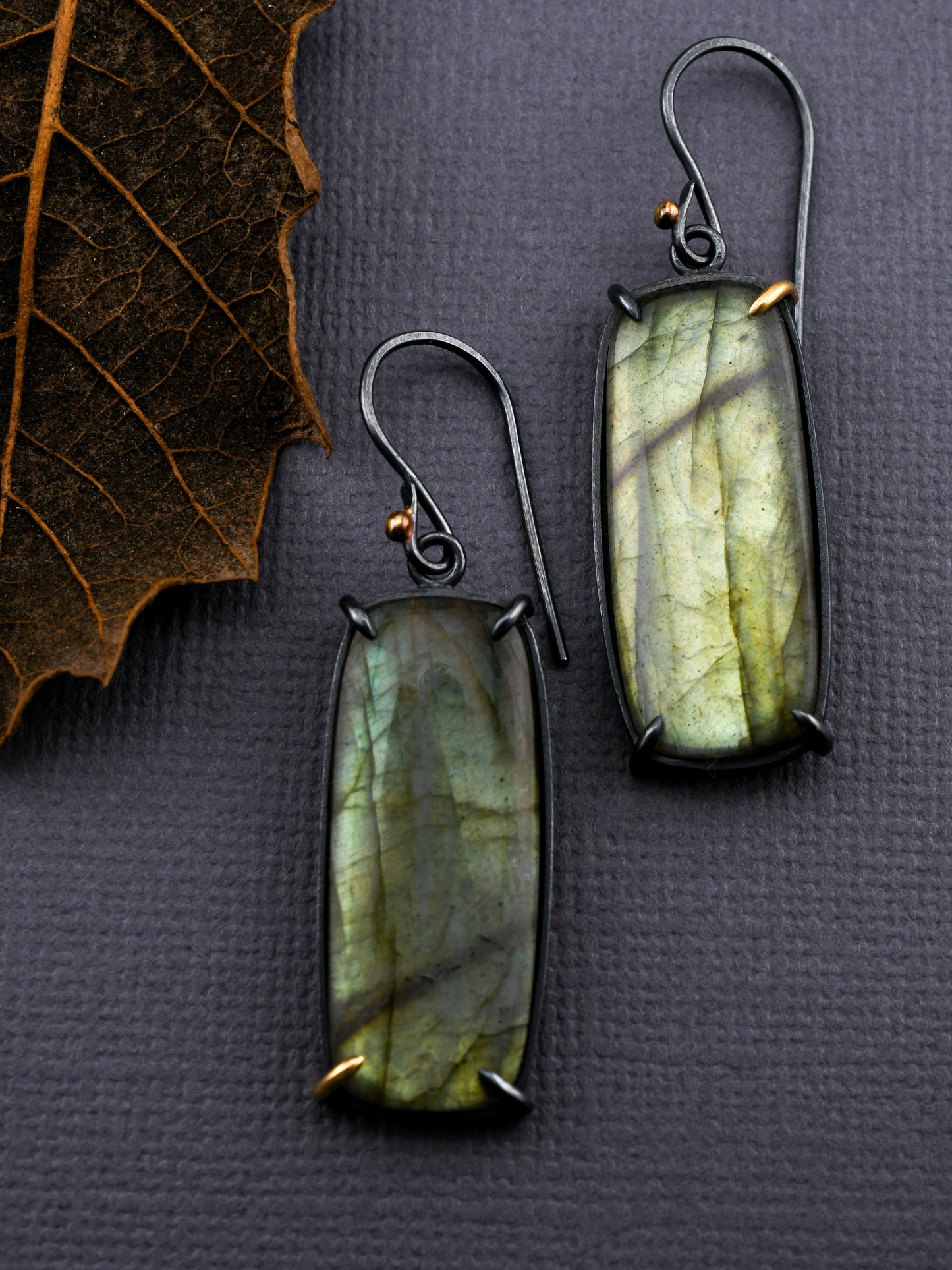 Green stone earrings on a textured gray surface with a leaf.