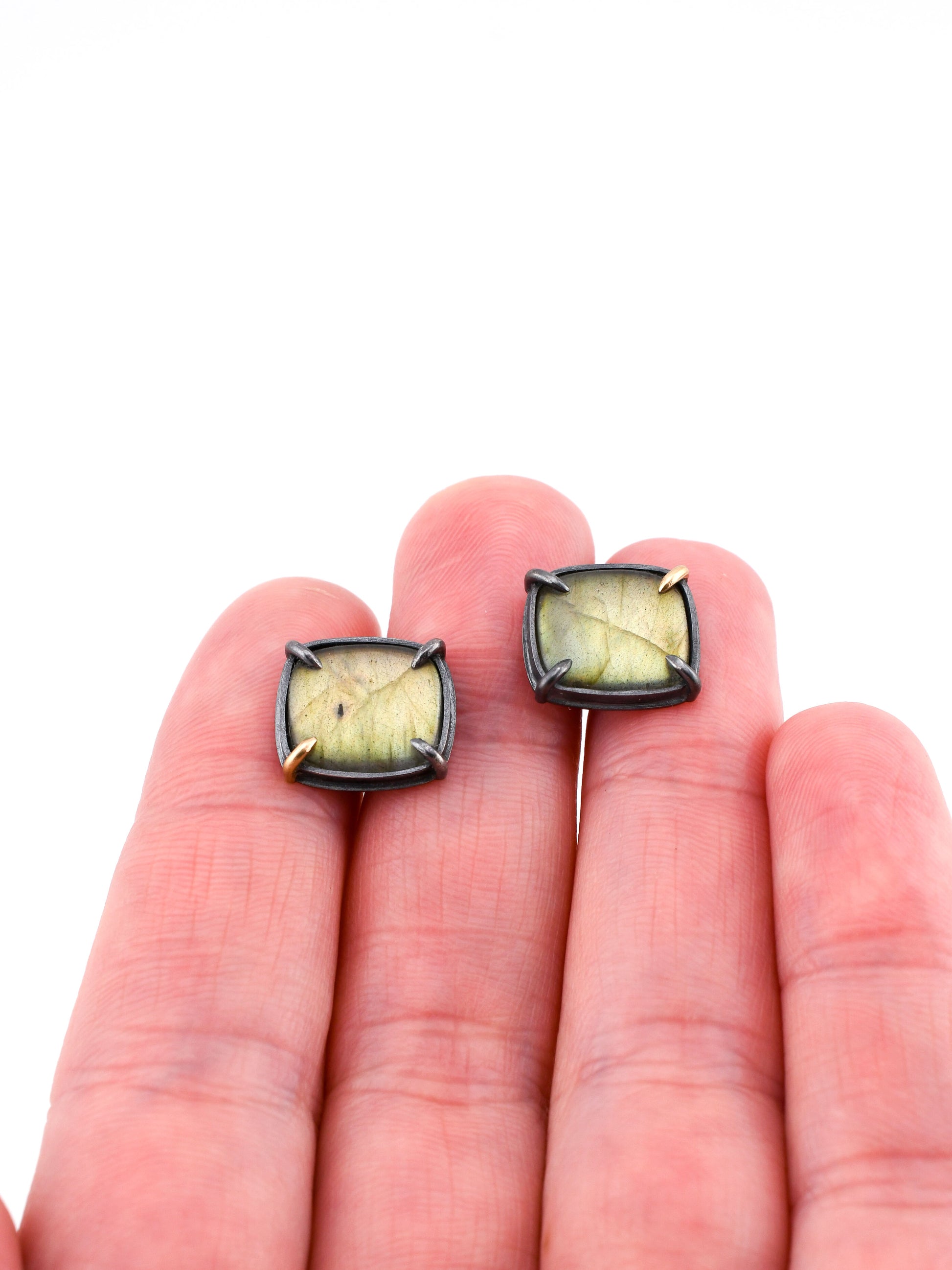 Pair of square stud earrings held between fingers on a white background
