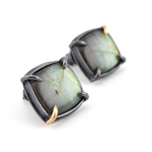 Pair of earrings with green gemstones and black metal frames on a white background