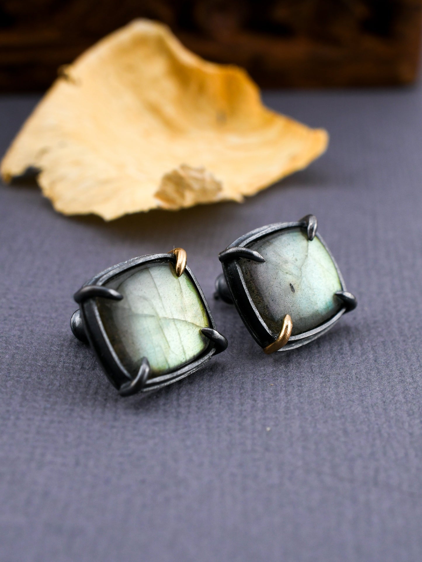 Pair of black-framed earrings with green gemstones on a gray surface.