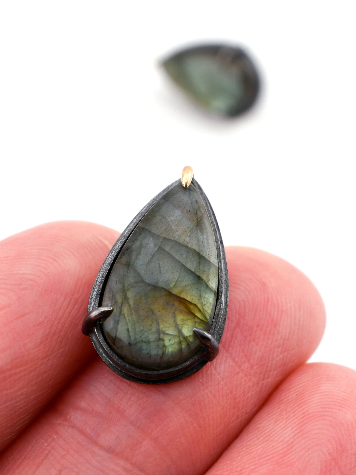 Teardrop-shaped labradorite stone held between fingers on a white background