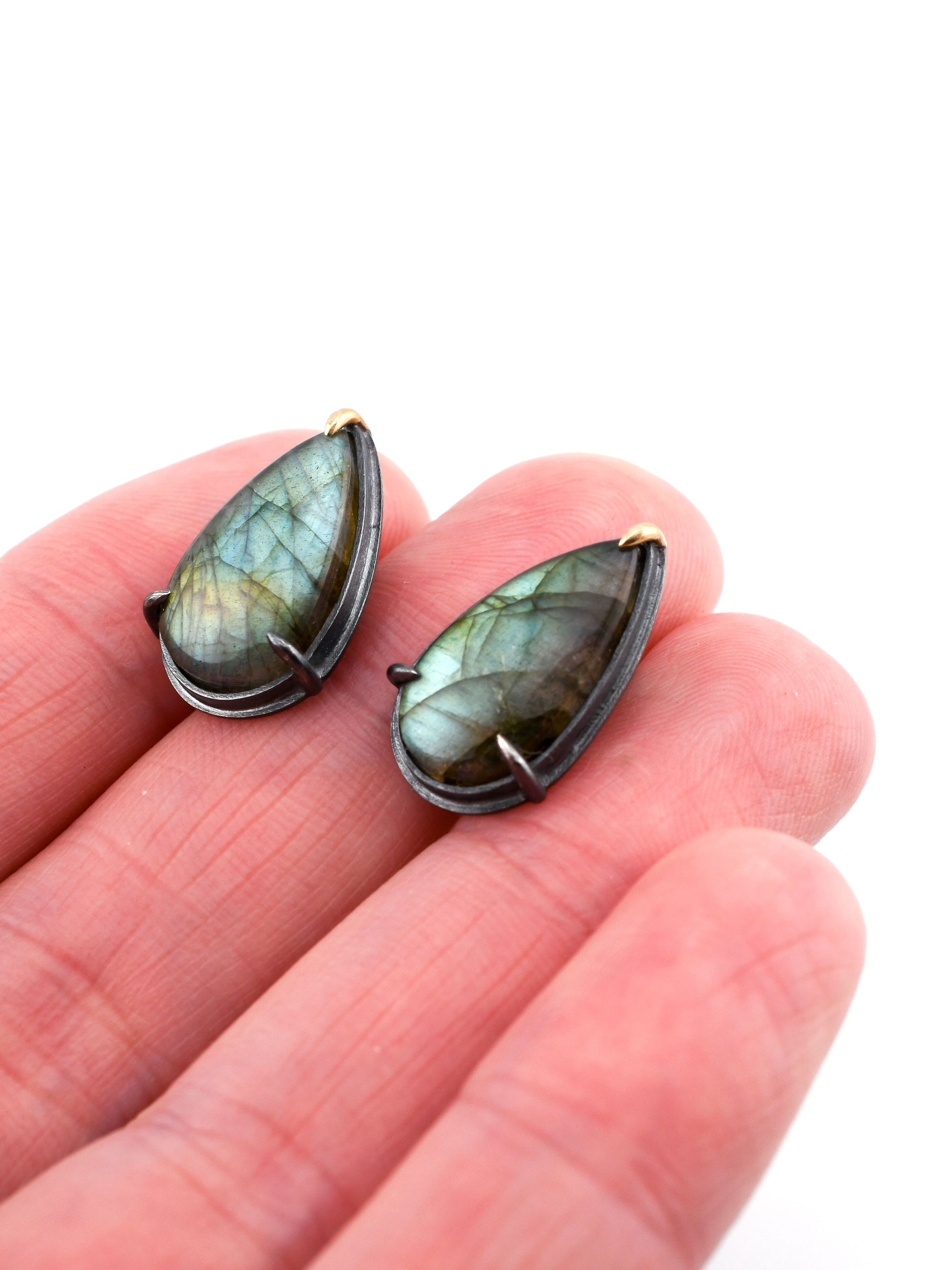Teardrop-shaped labradorite stones held between fingers on a white background