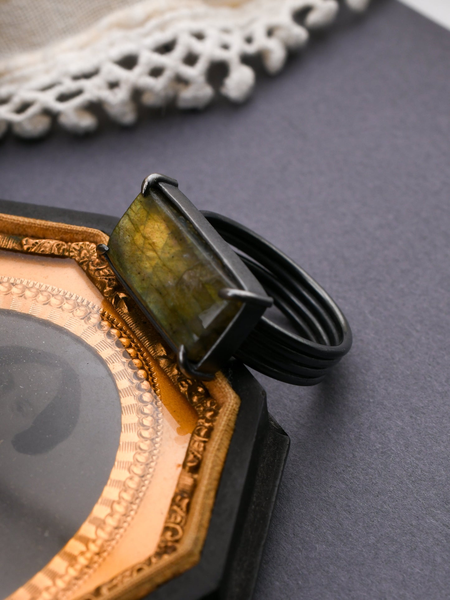 Rectangular green stone ring propped against a decorative frame on a dark gray background