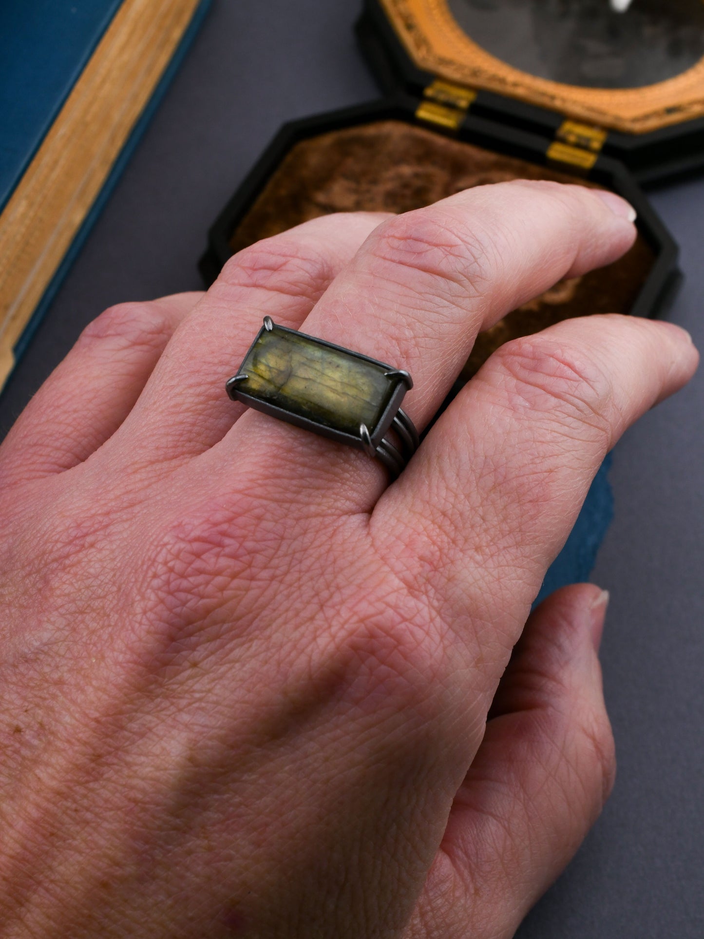 Hand wearing a ring with a green stone, set against a dark background