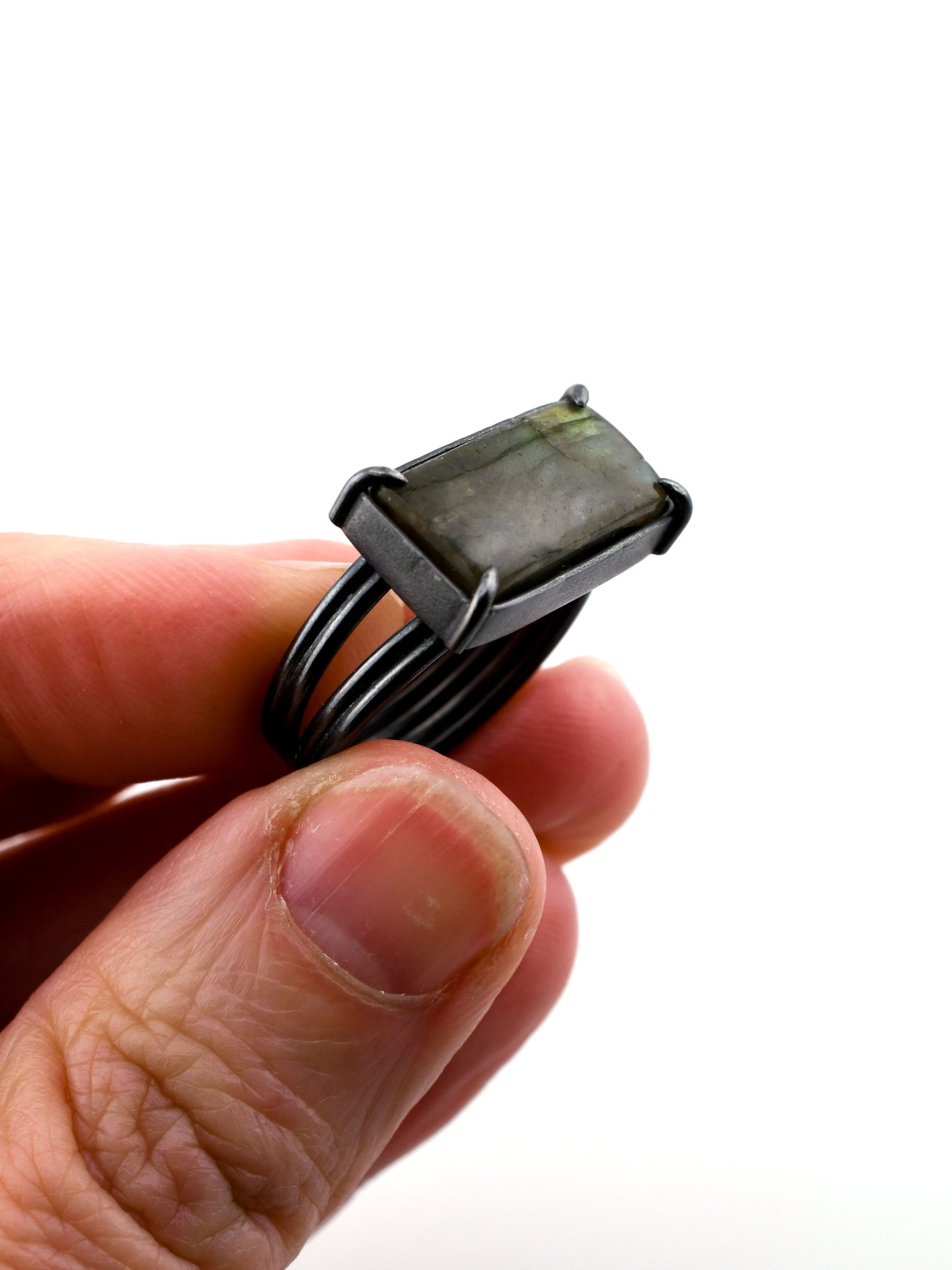 Hand holding a black metal ring with a rectangular stone on a white background