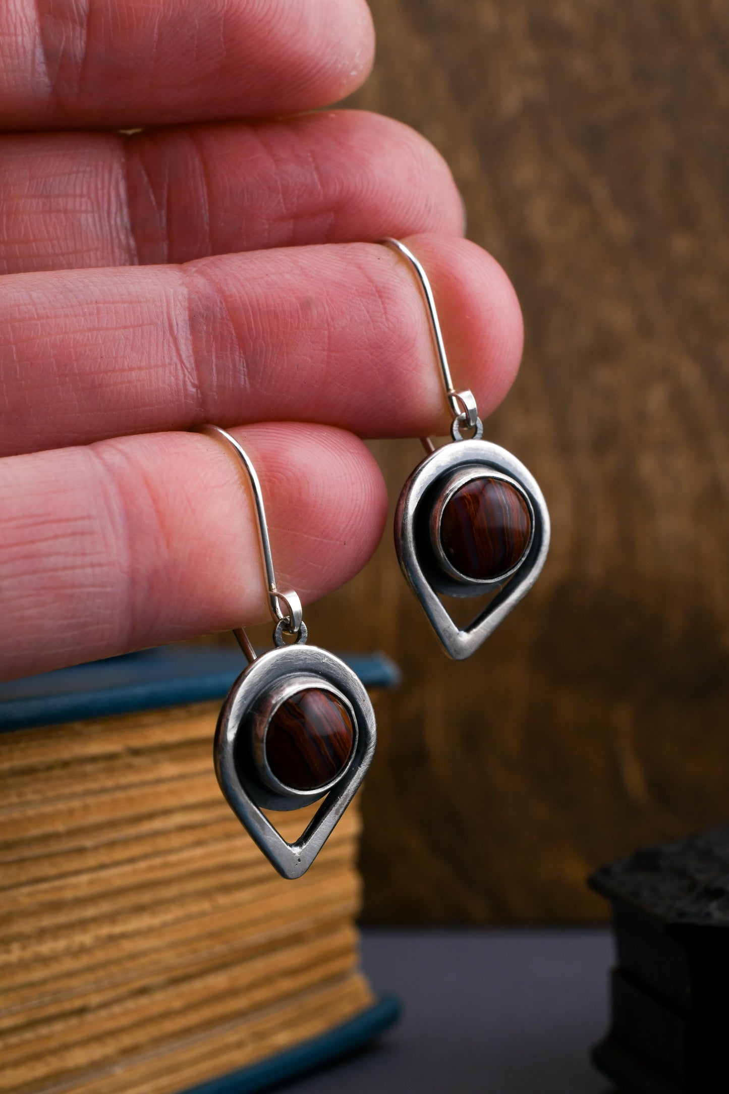 Silver earrings with banded agate gemstones held between fingers against a blurred background
