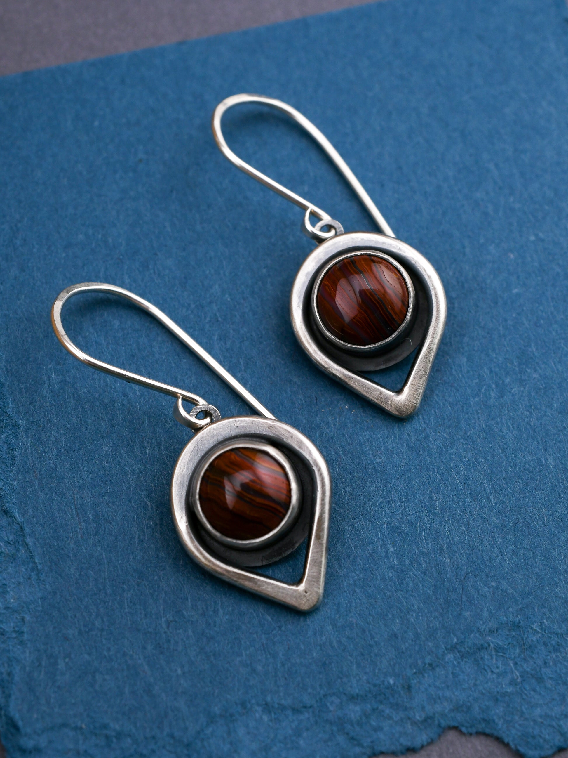 Silver earrings with banded red gemstones on a blue textured background