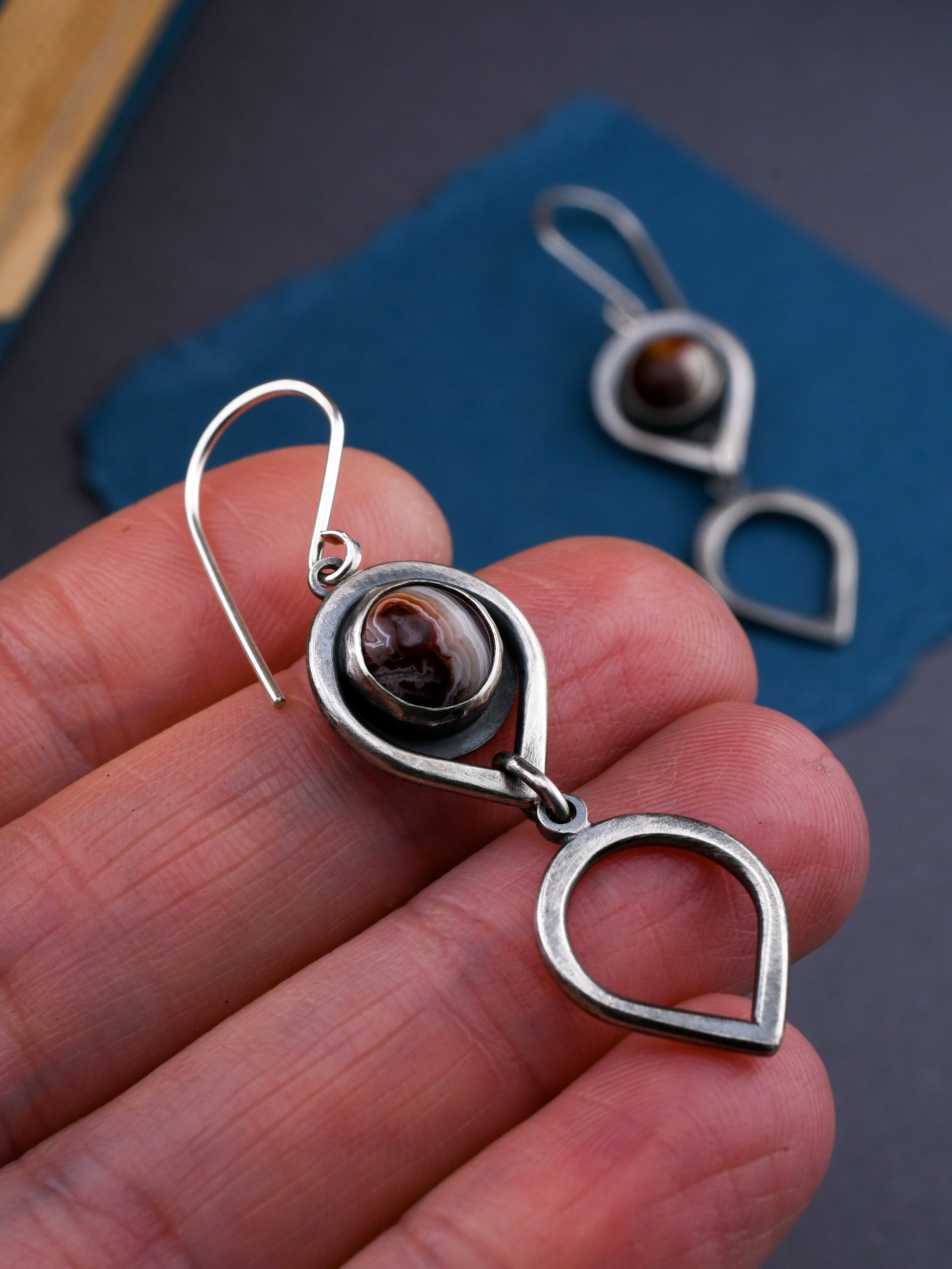 Silver earrings with banded red gemstones held in a hand against a dark background