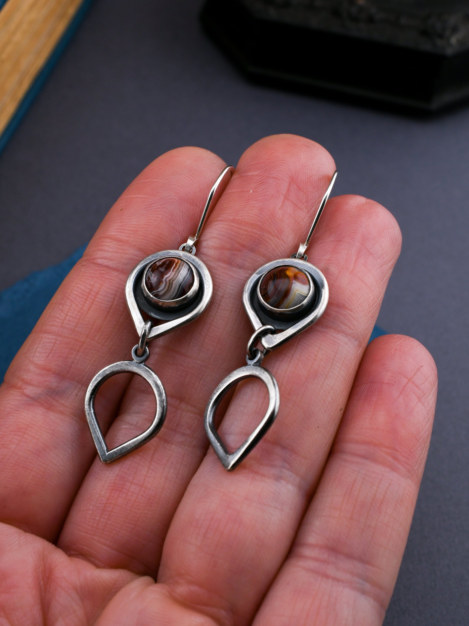 Silver earrings with gemstones held in a hand against a neutral background