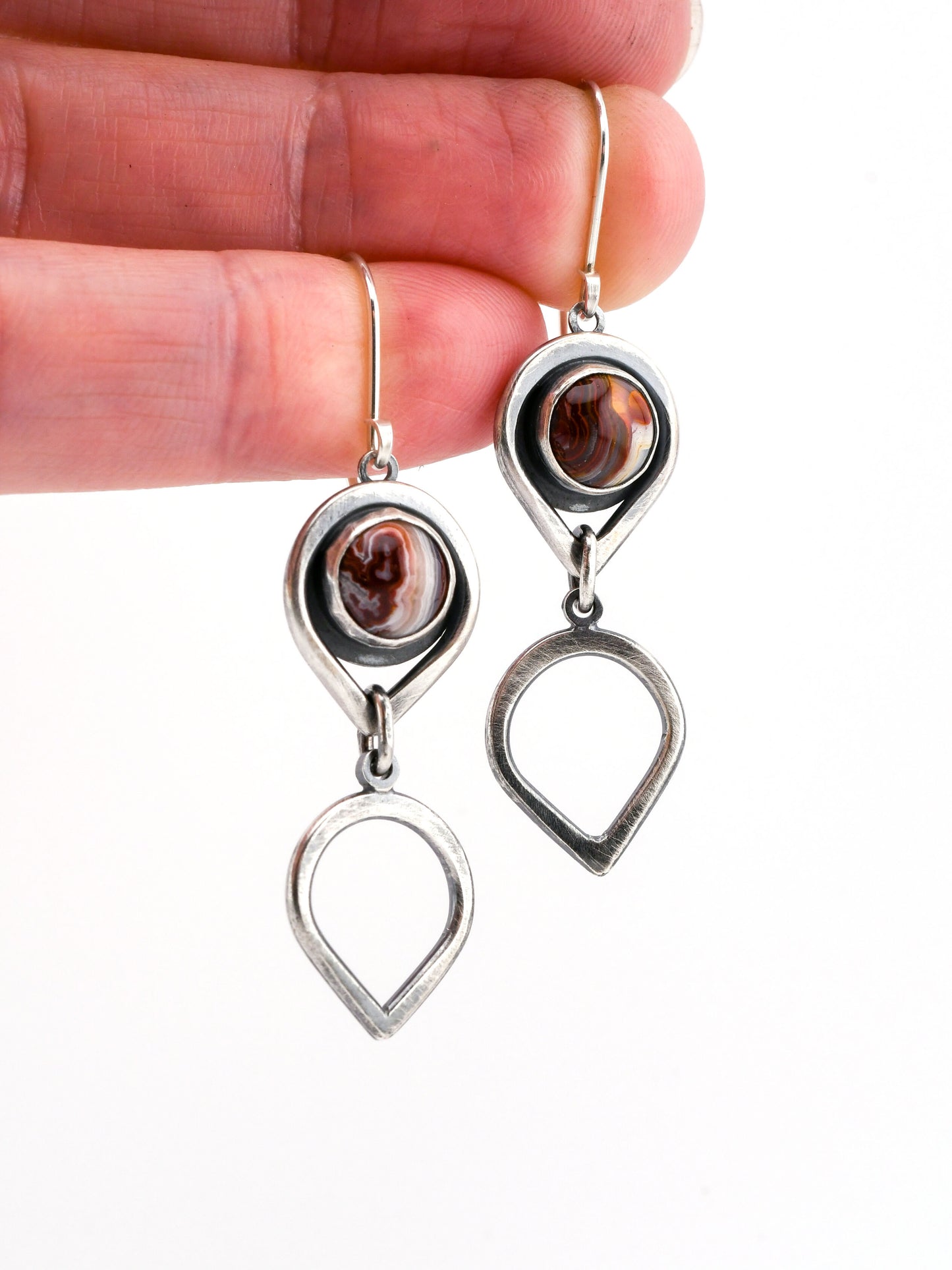 Silver earrings with red stones held between fingers on a white background
