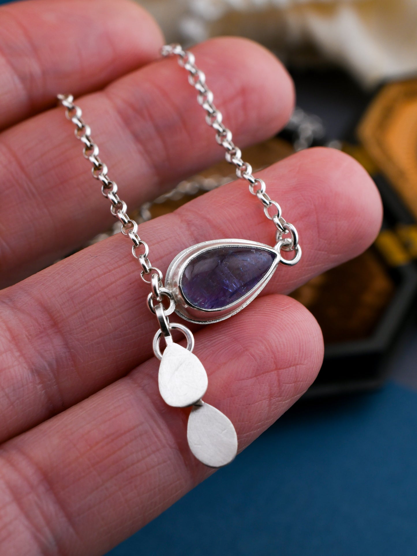 Silver necklace with a purple teardrop pendant held in a hand.