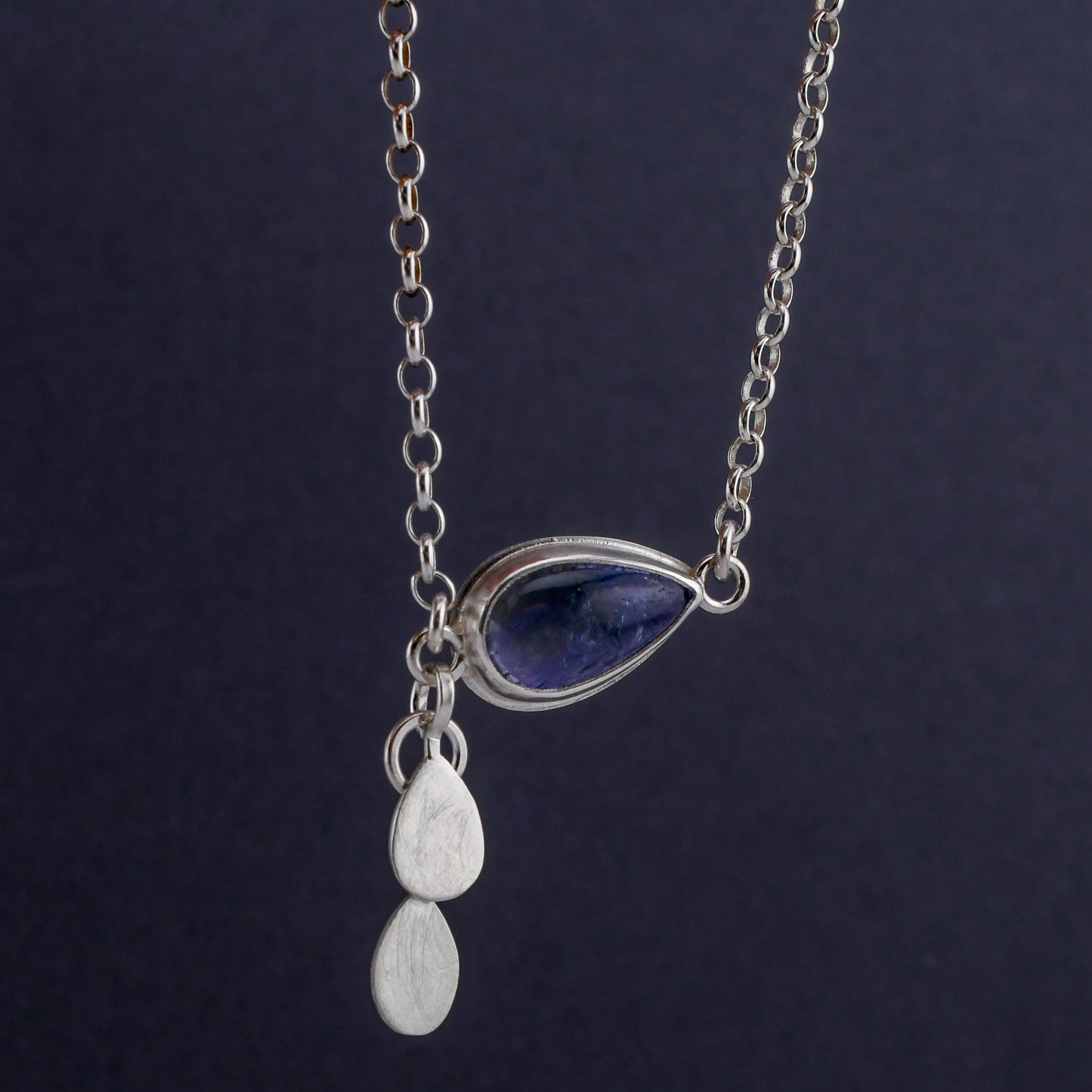 Silver necklace with a teardrop pendant on a dark background