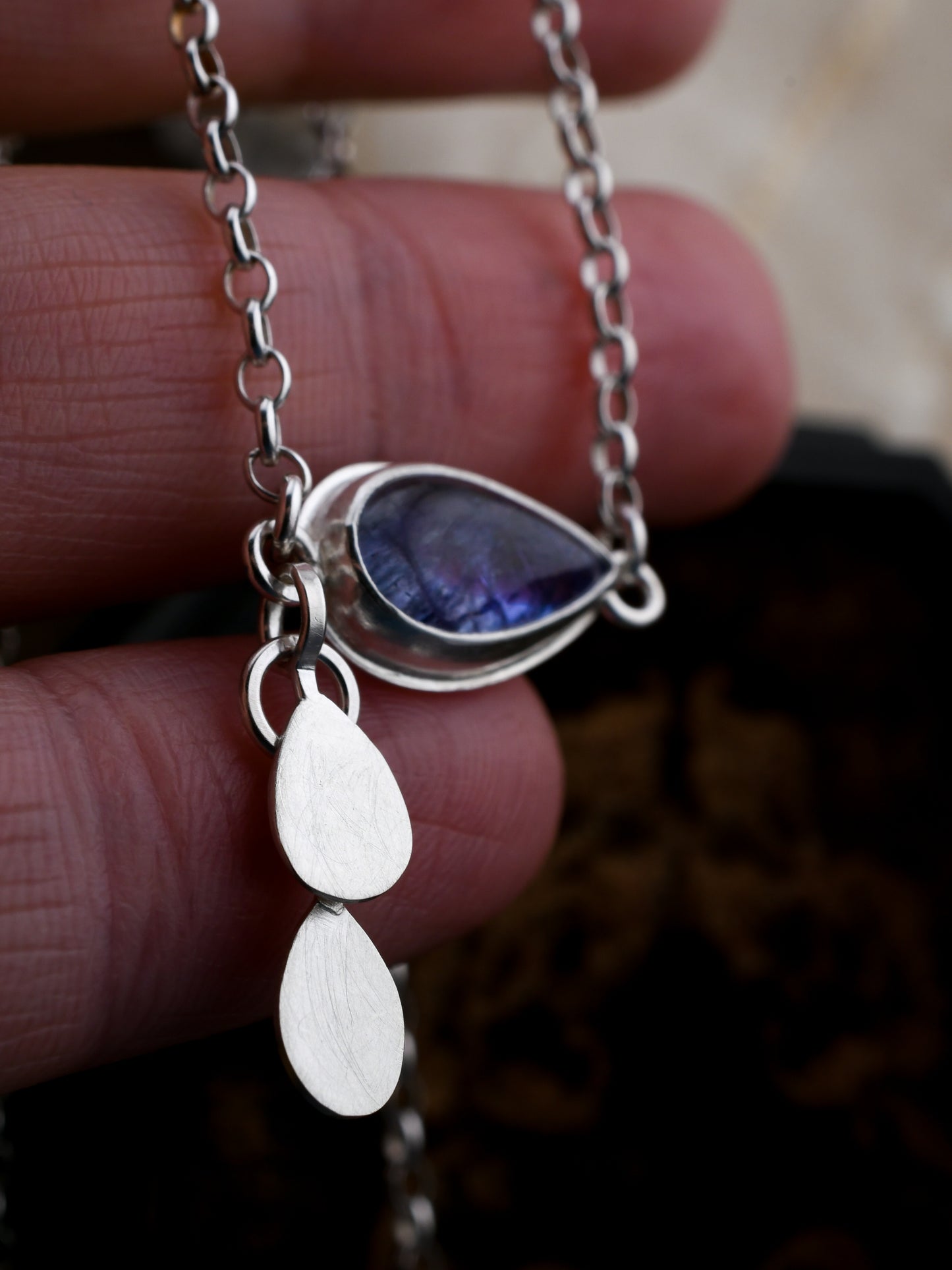 Silver necklace with a pendant held between fingers