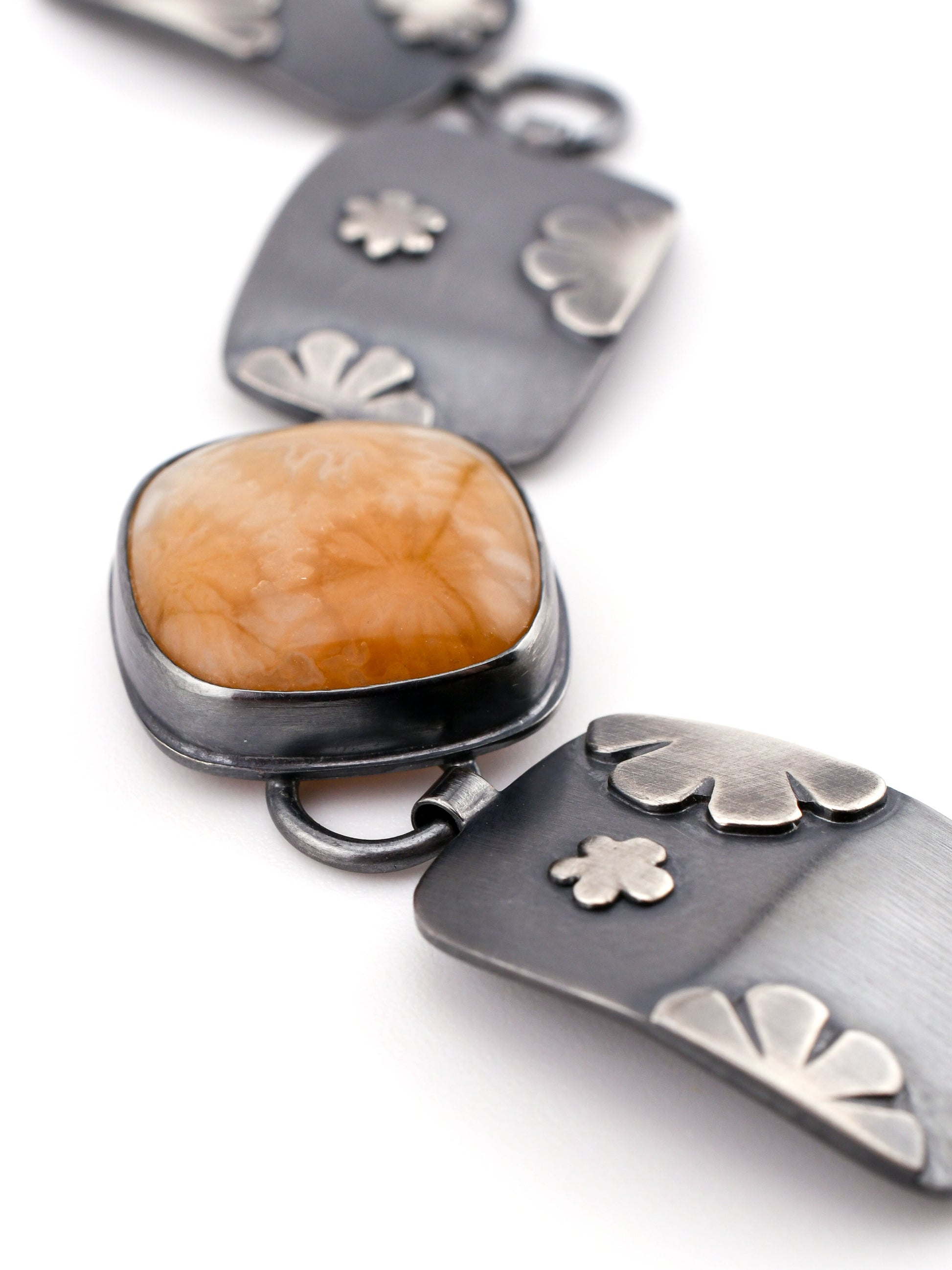 close up of golden square stone and links of a bracelet on a white background
