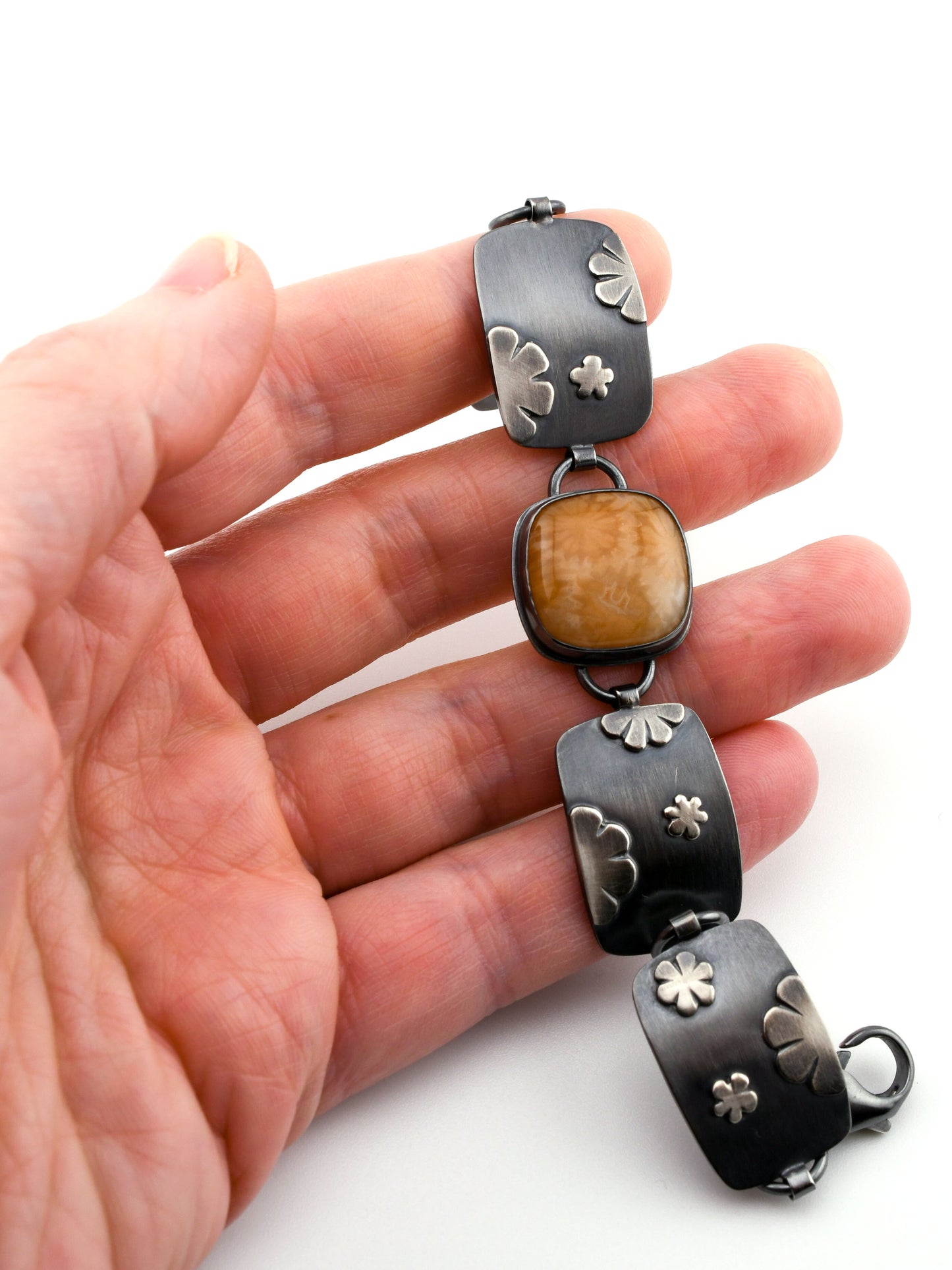 Hand holding a unique silver and stone bracelet on a white background