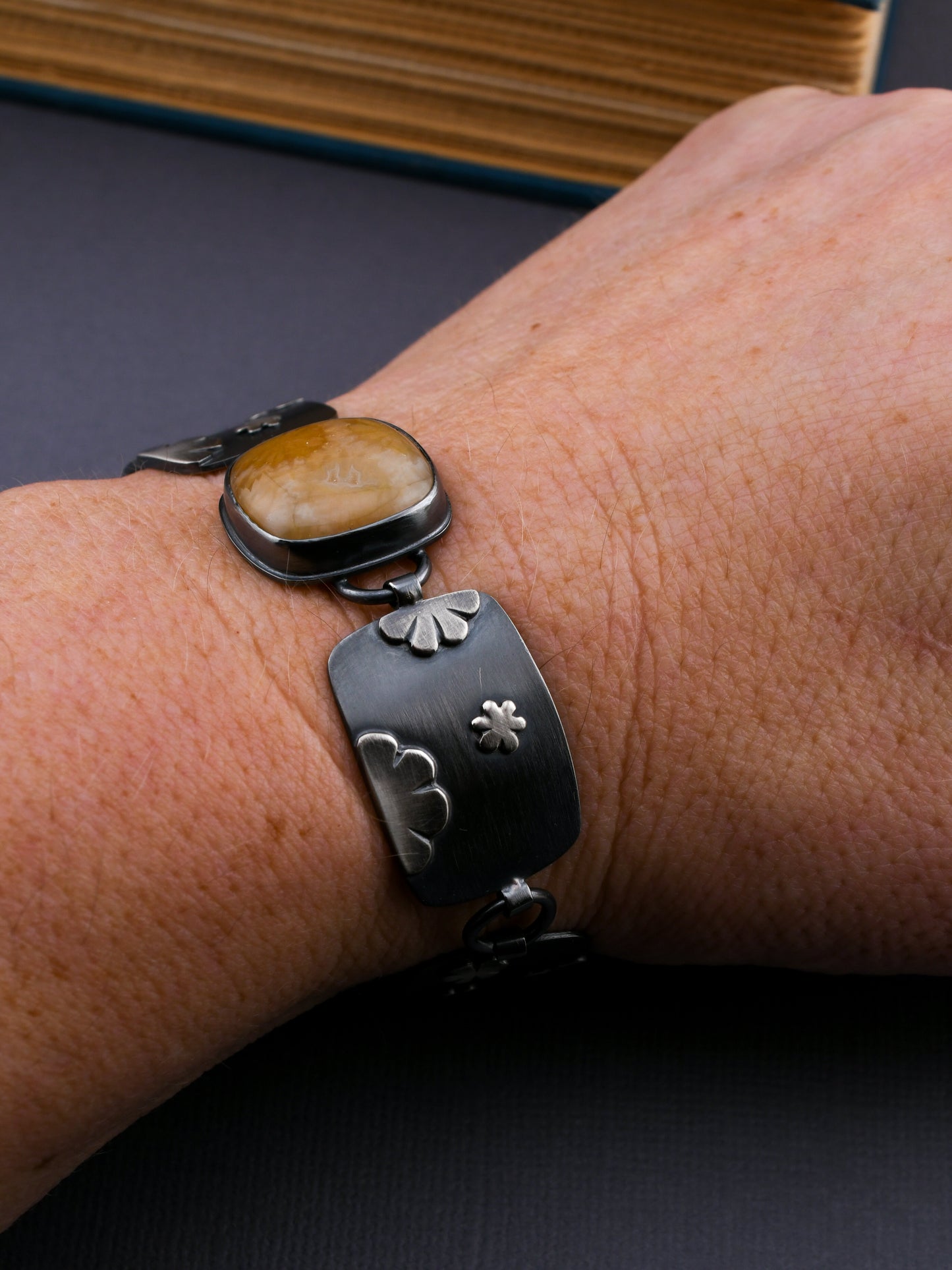 Black flower patterned bracelet with gold-colored stone on a dark gray background