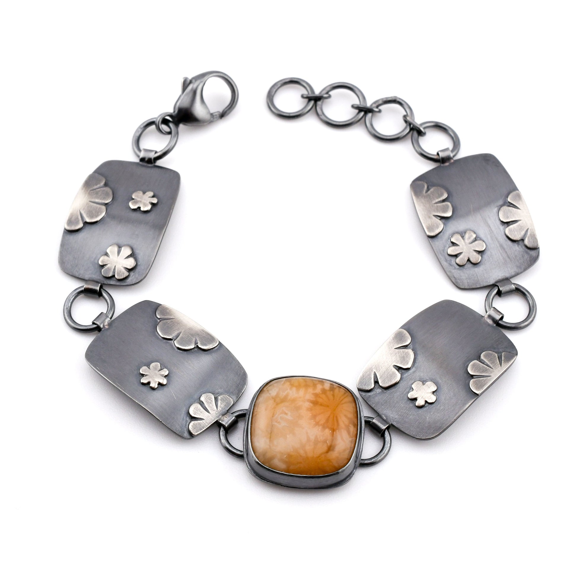 Silver bracelet with floral designs and a central amber-colored stone on a white background