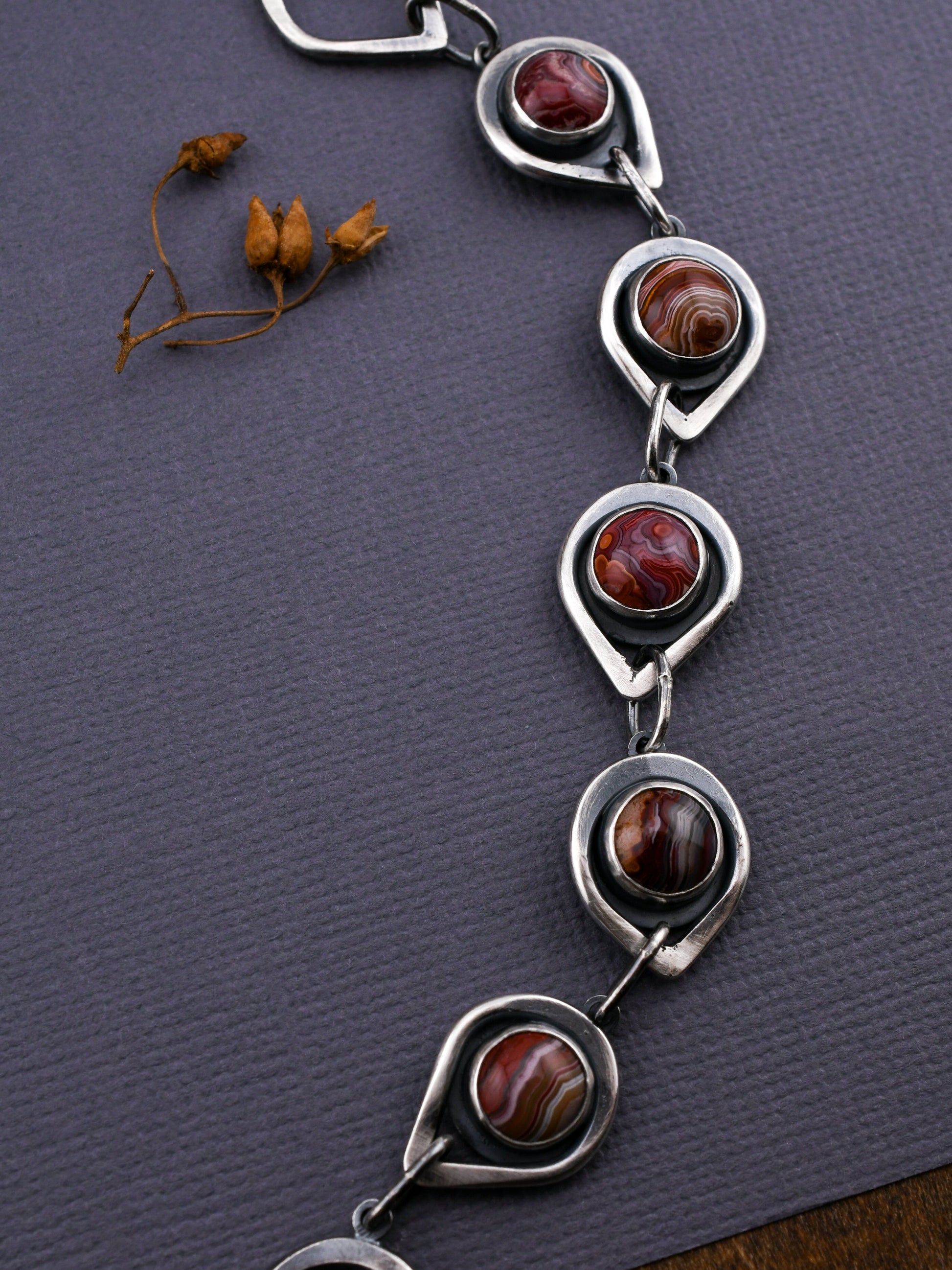 Silver bracelet with circular designs and embedded stones on a textured gray surface.