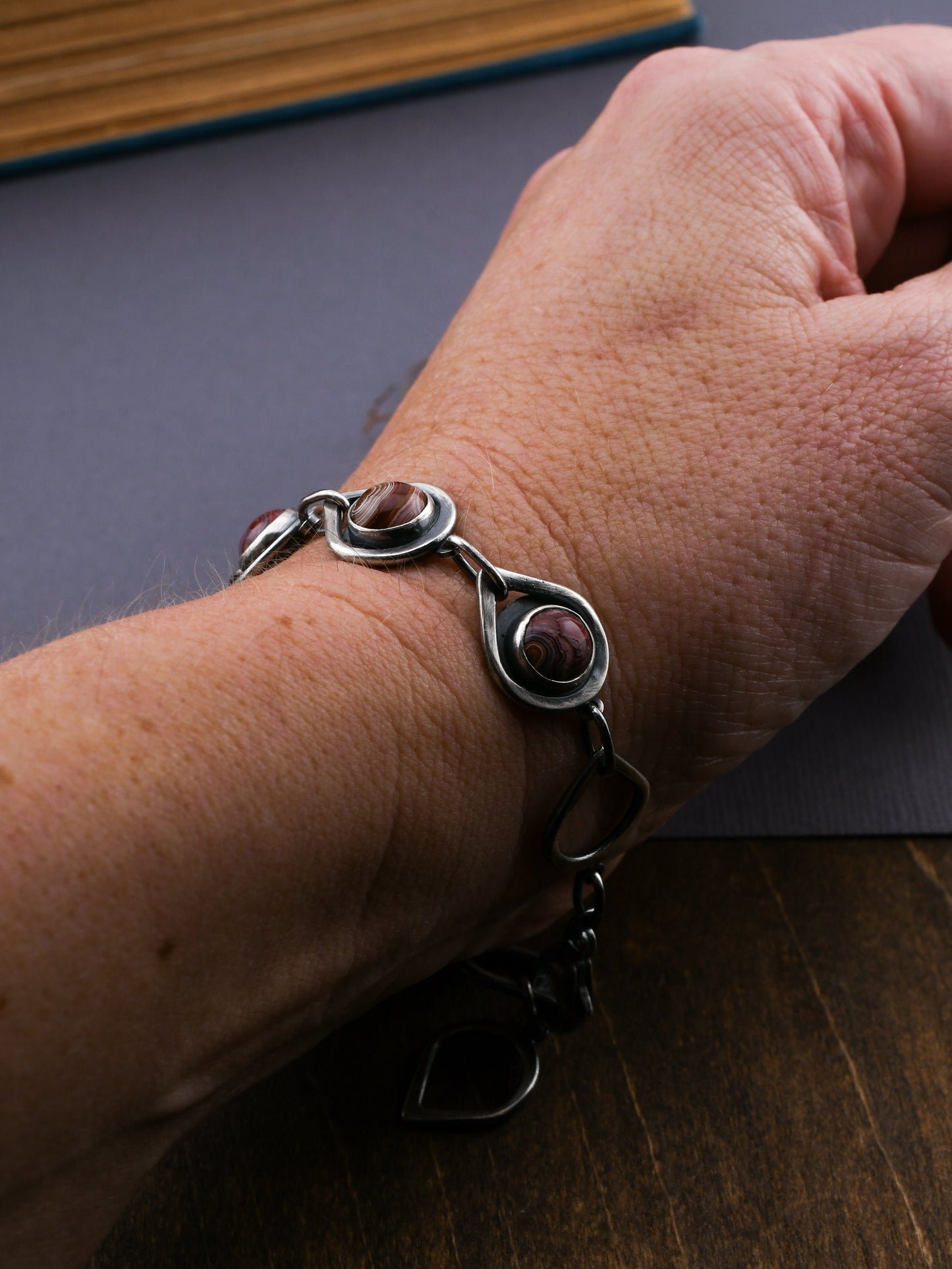Silver bracelet with red stones on a wrist, with a book in the background