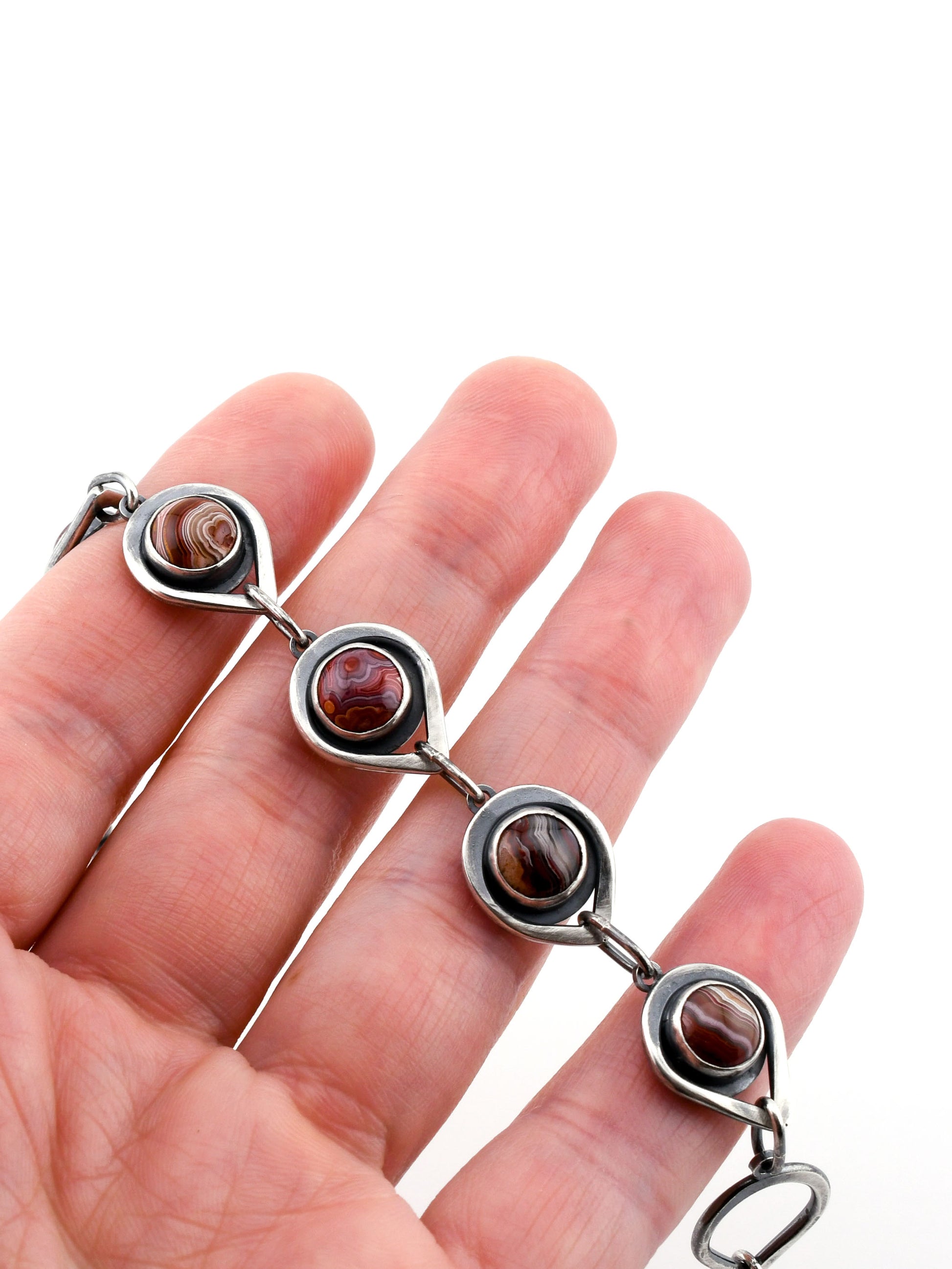 Silver bracelet with red stones held in a hand on a white background
