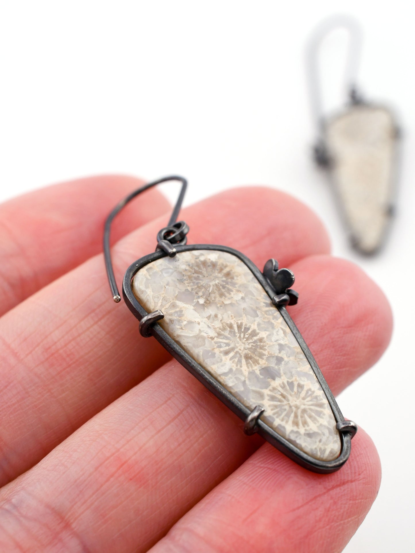 floral stone earrings held between fingers with a blurred background