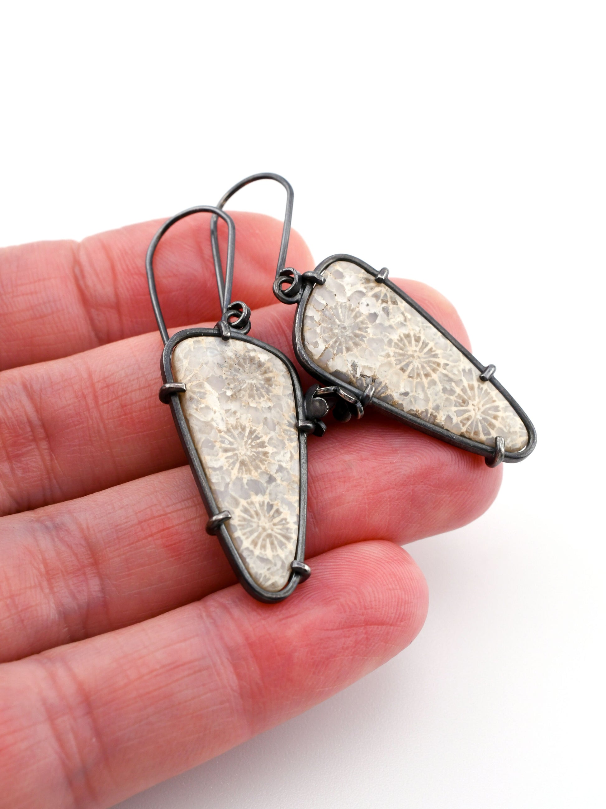 Decorative earrings held in a hand against a white background