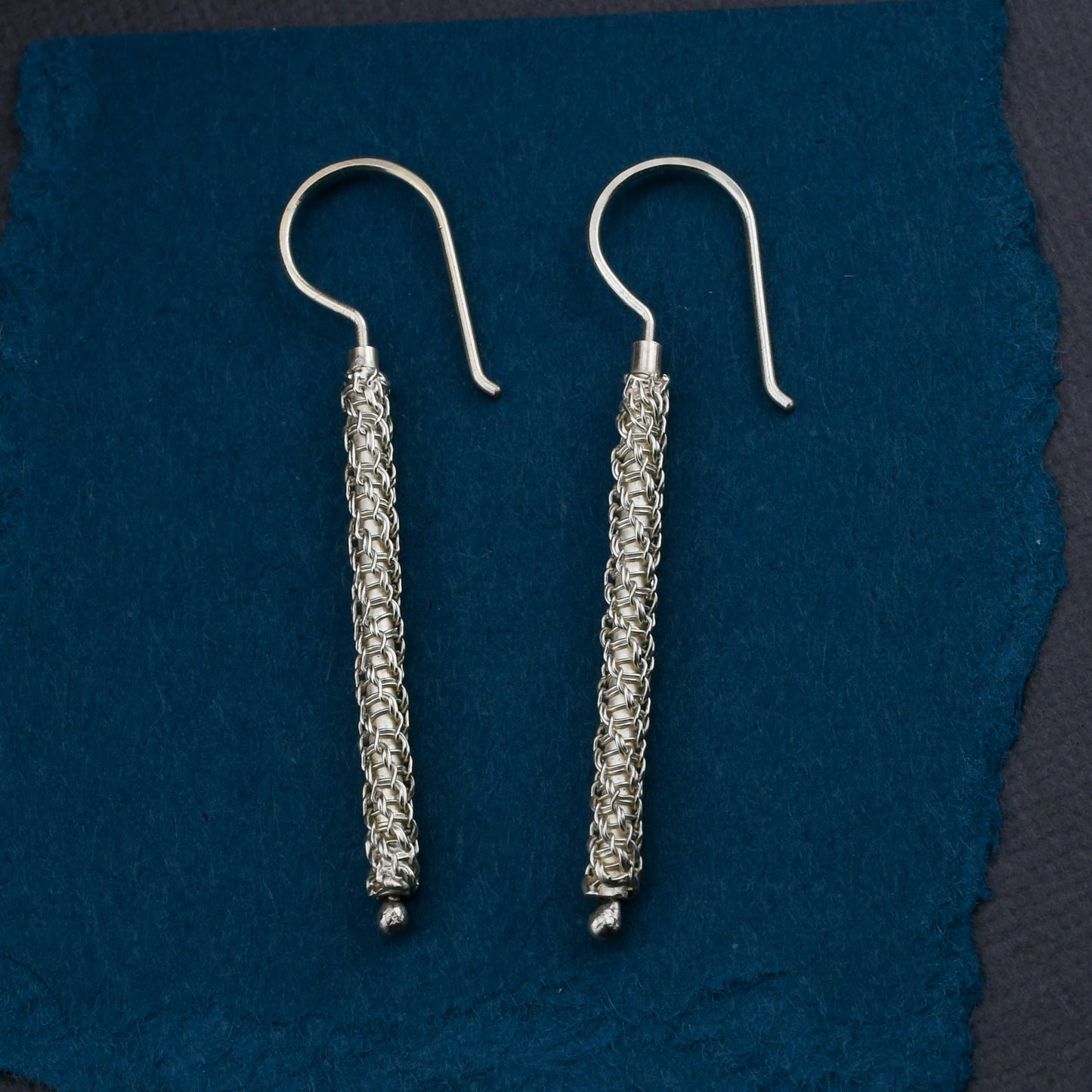 Pair of woven chainmaille earrings on a blue fabric background