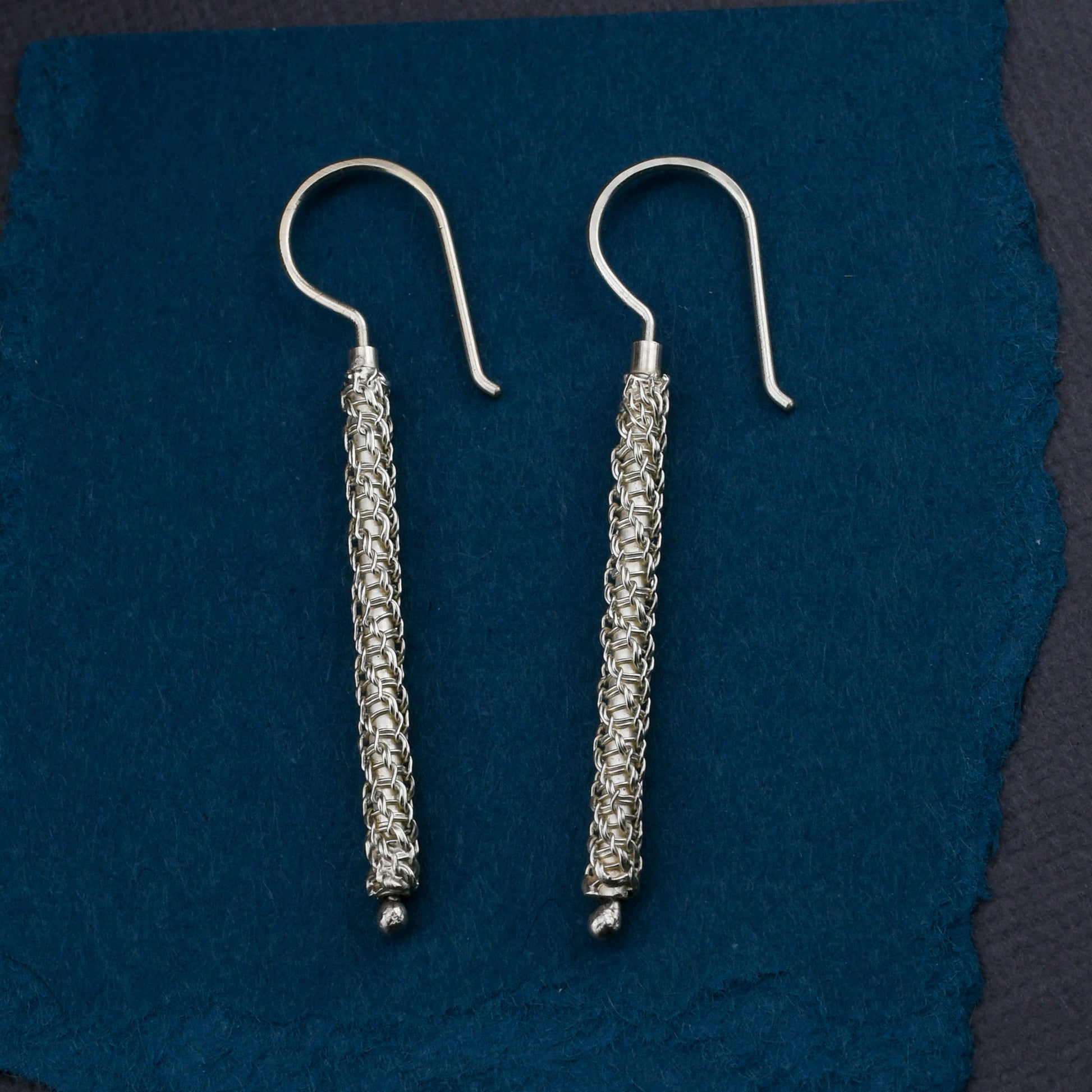 Pair of woven chainmaille earrings on a blue fabric background