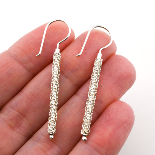 Silver wire-wrapped earrings held between fingers on a white background