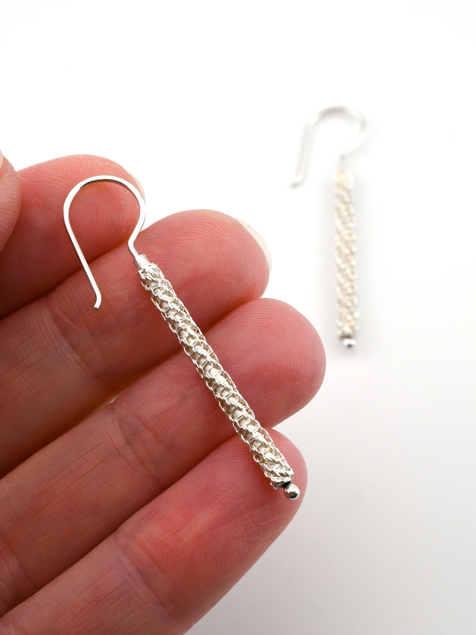 Silver textured earring held between fingers with a plain background