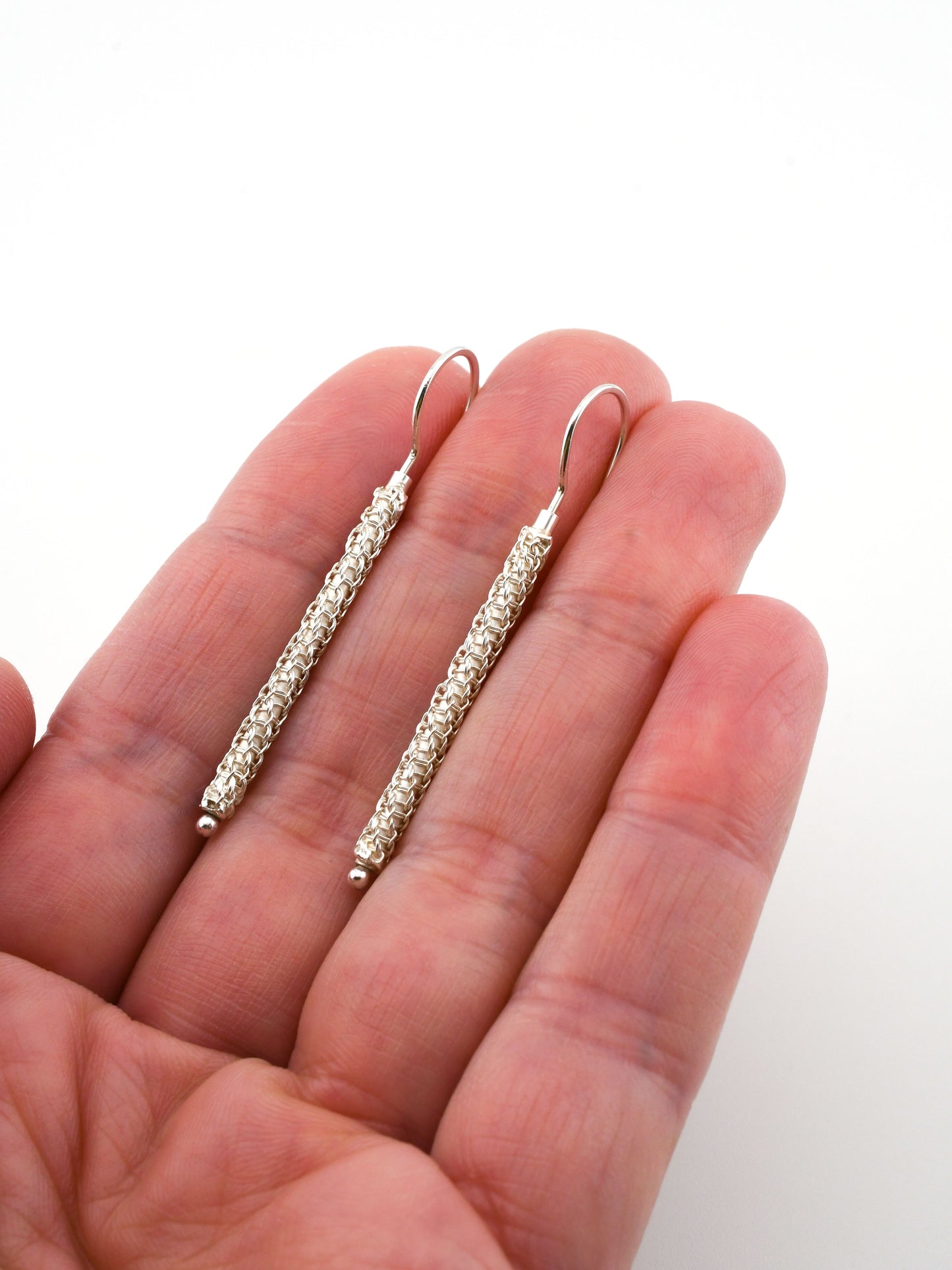 Silver earrings held in a hand against a white background