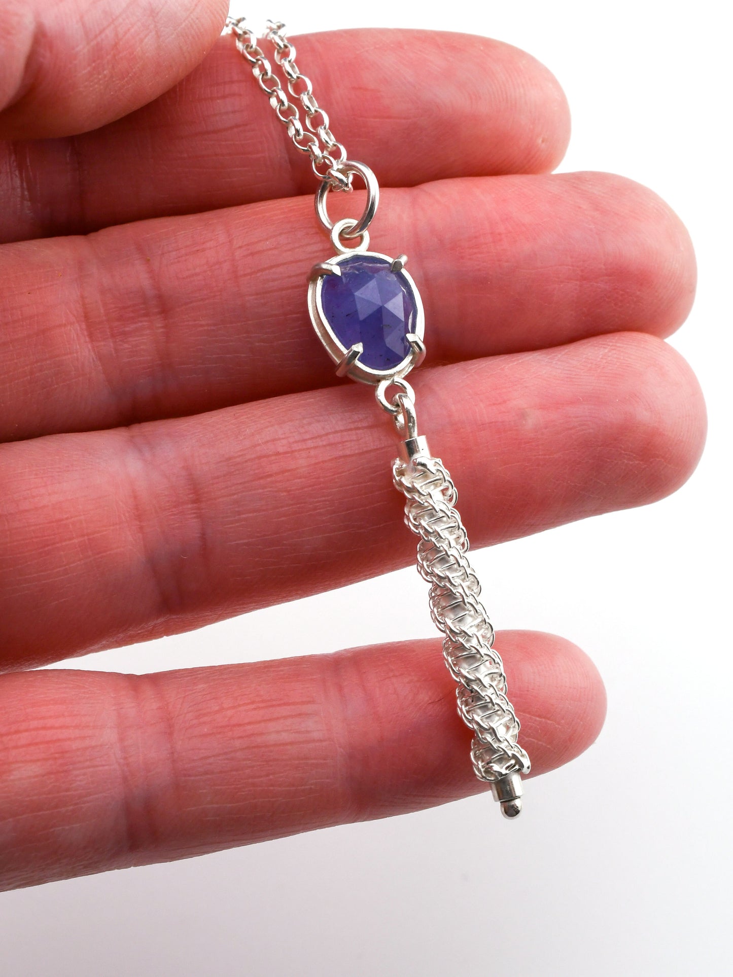 Silver necklace with a blue pendant held between fingers on a white background