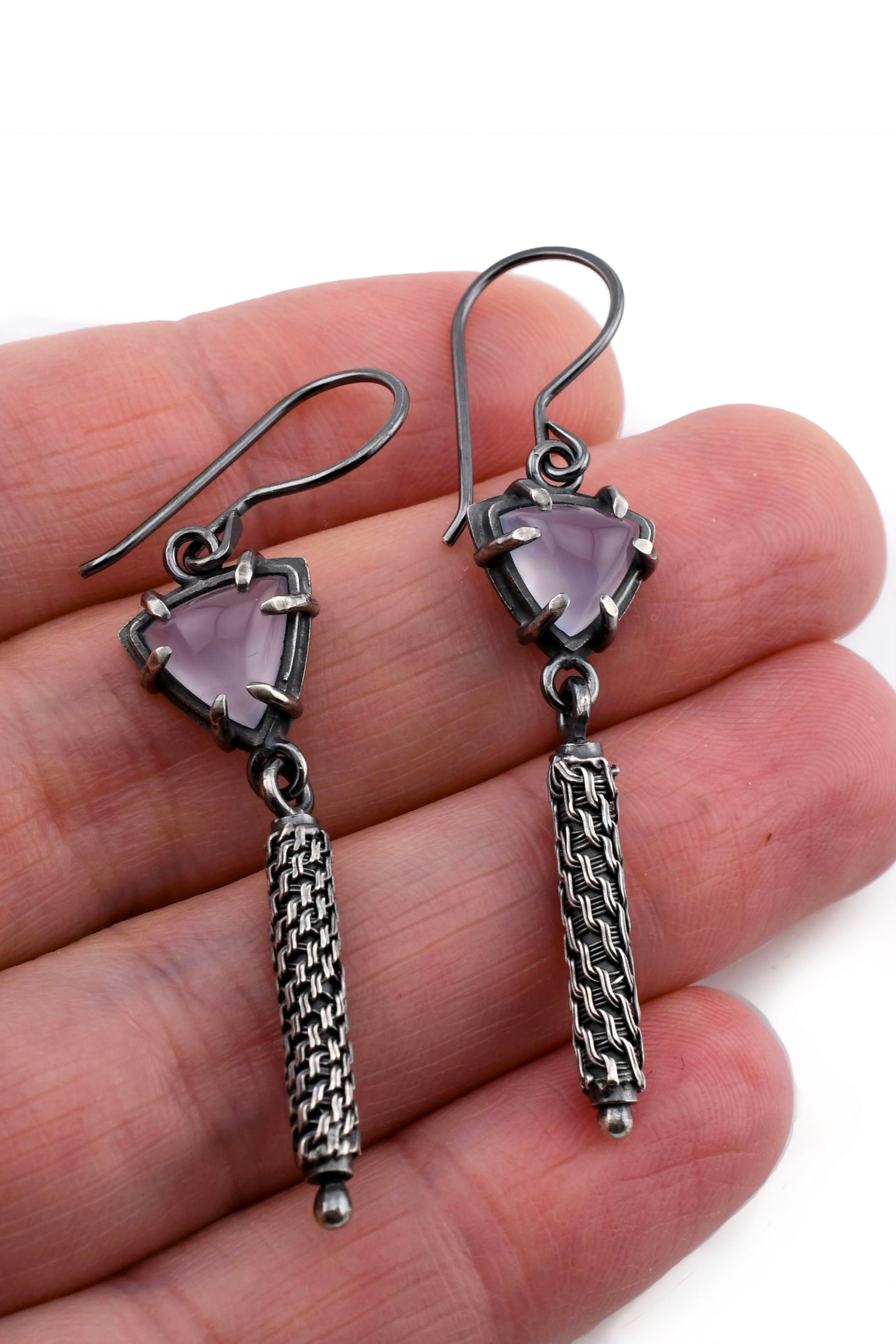 Silver earrings with purple gemstones held in a hand on a white background