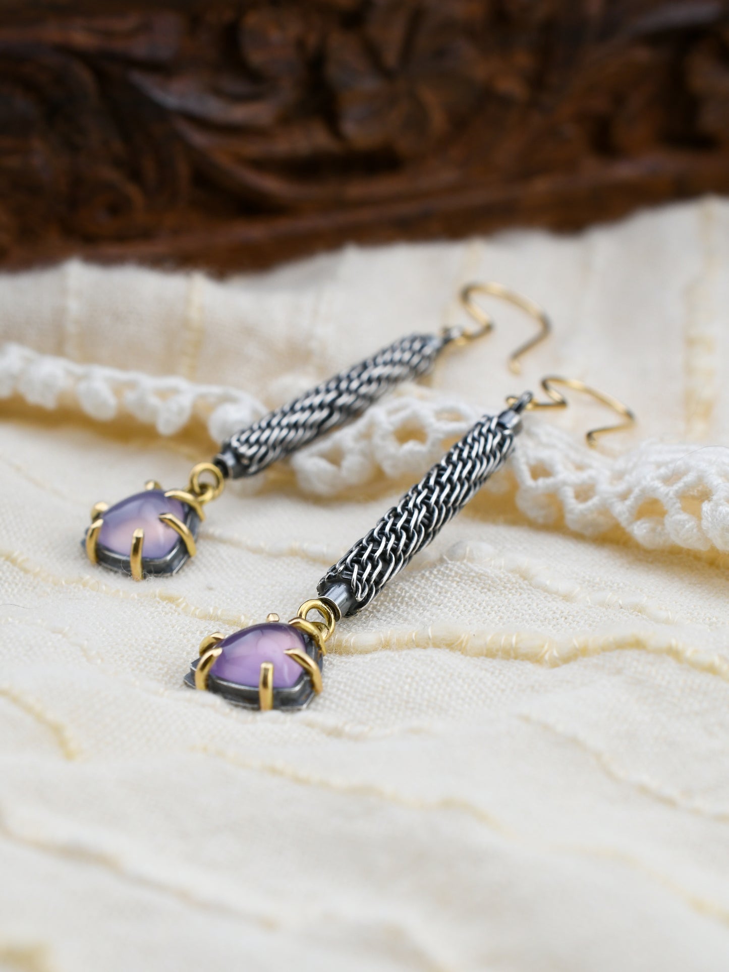 Pair of earrings with purple gemstones on a textured fabric background