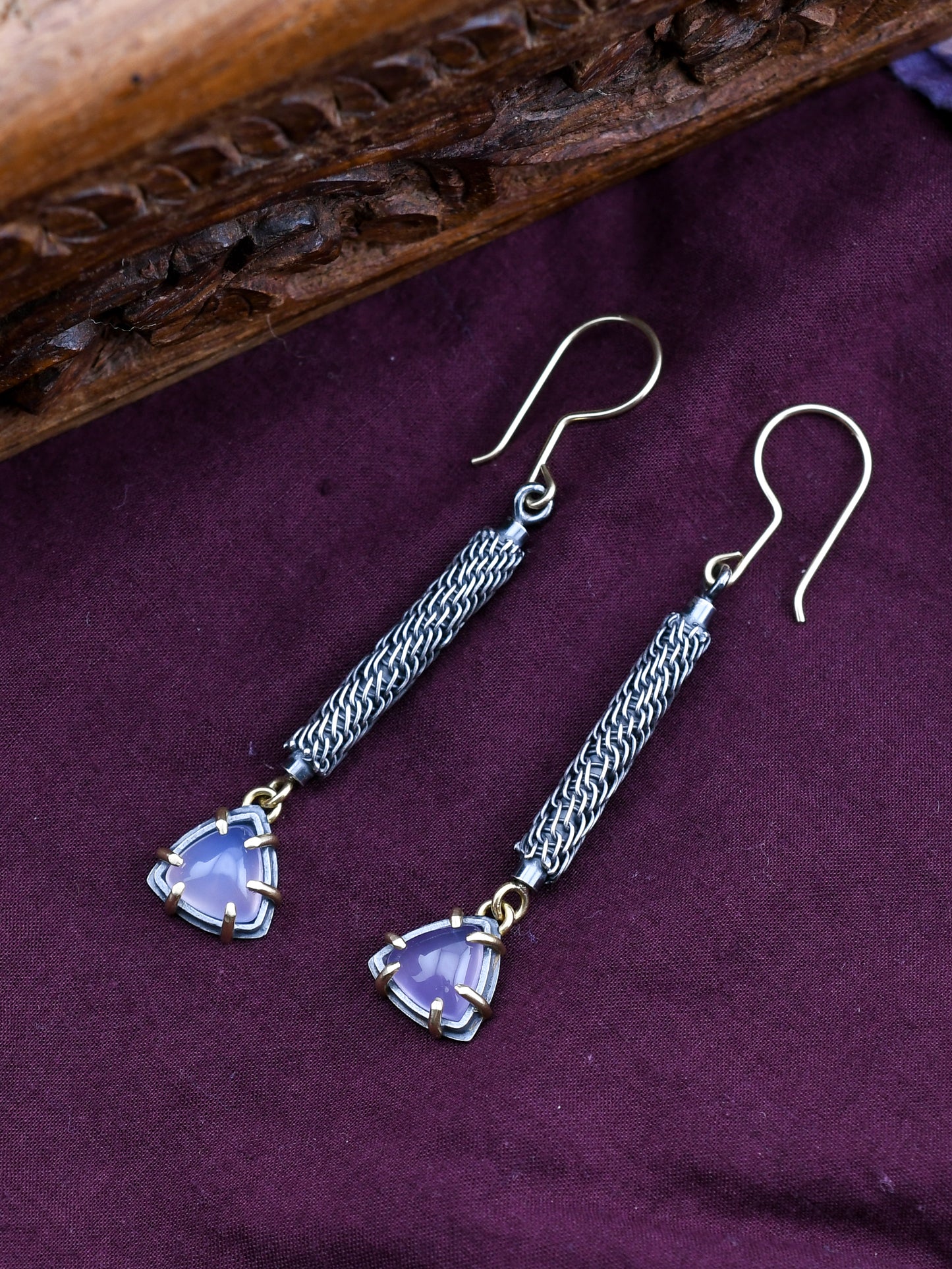 Silver earrings with purple triangle-shaped stones on a purple fabric background
