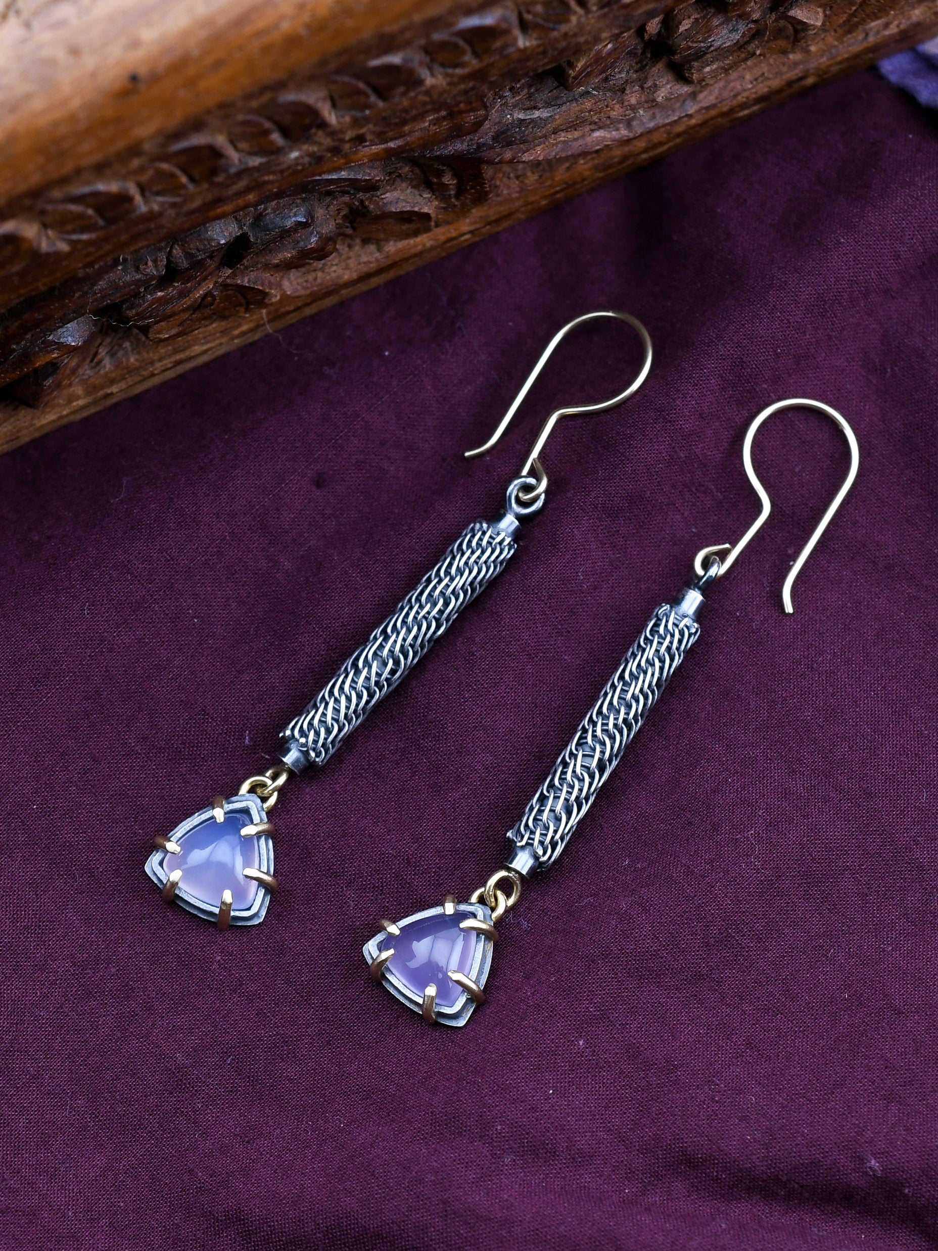 Silver earrings with purple triangle-shaped stones on a purple fabric background