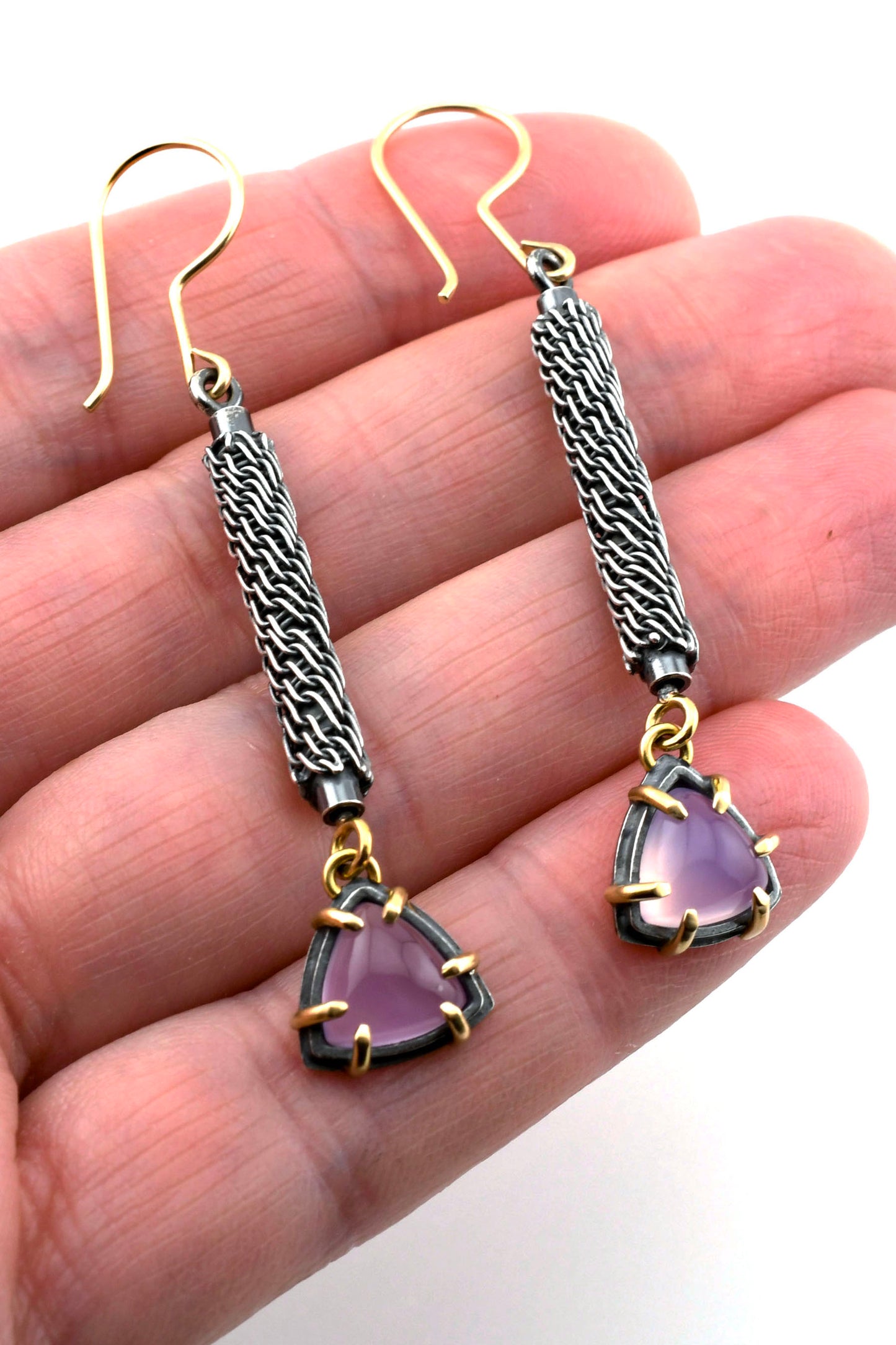 purple gemstone earrings held in a hand on a white background