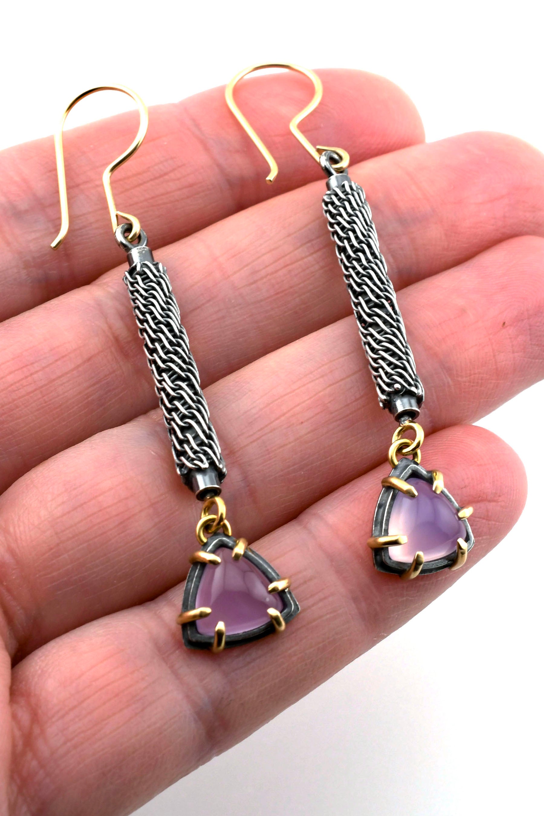 purple gemstone earrings held in a hand on a white background