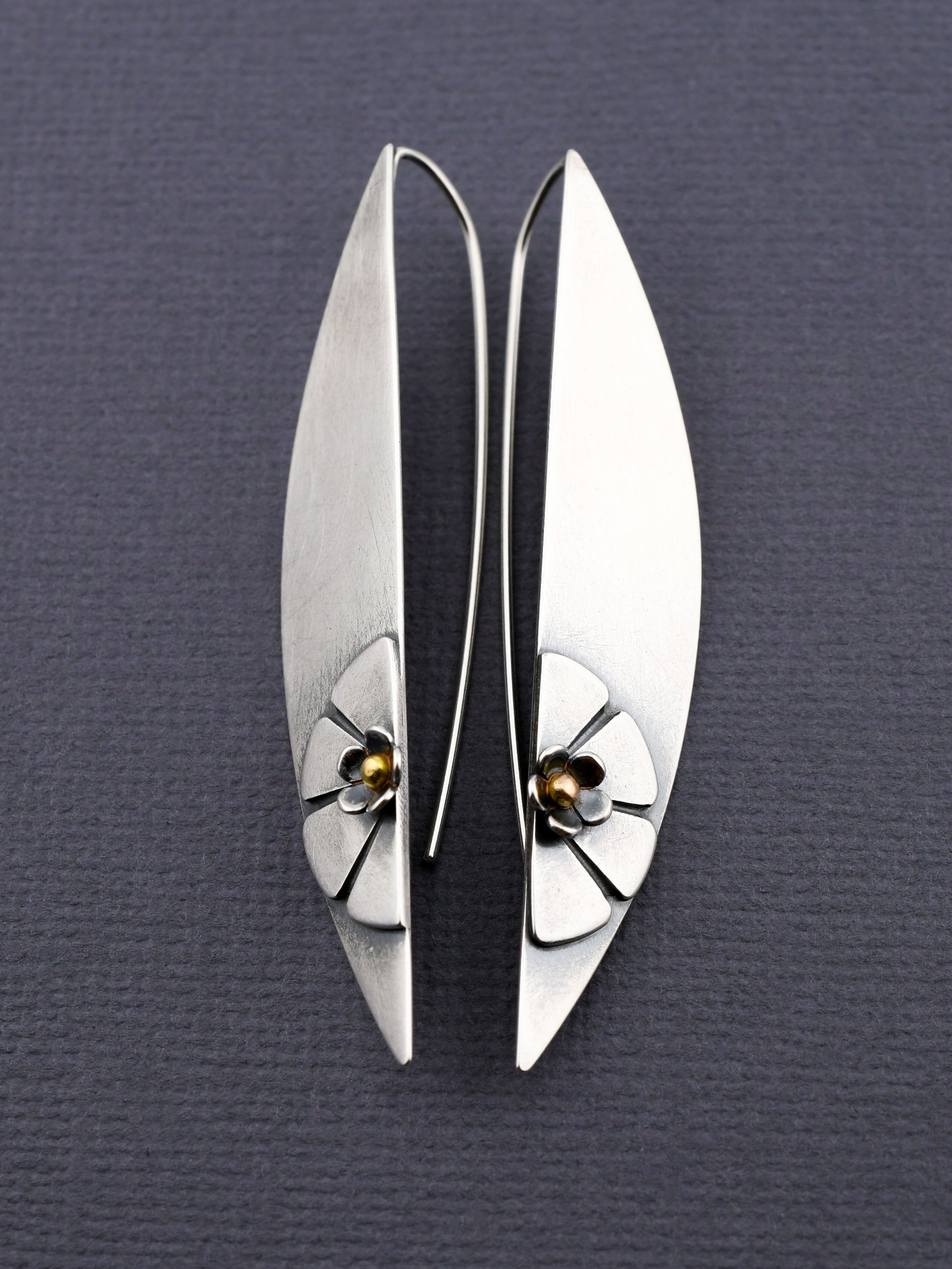Pair of silver earrings with floral designs on a gray background