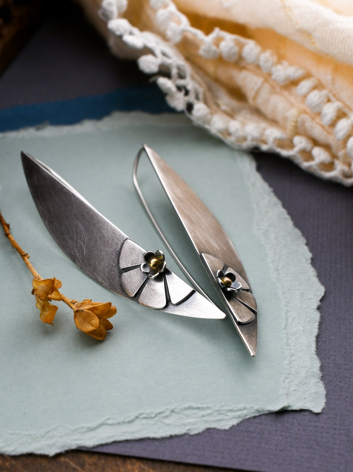 silver earrings with flower design on a textured background with dried flowers and lace