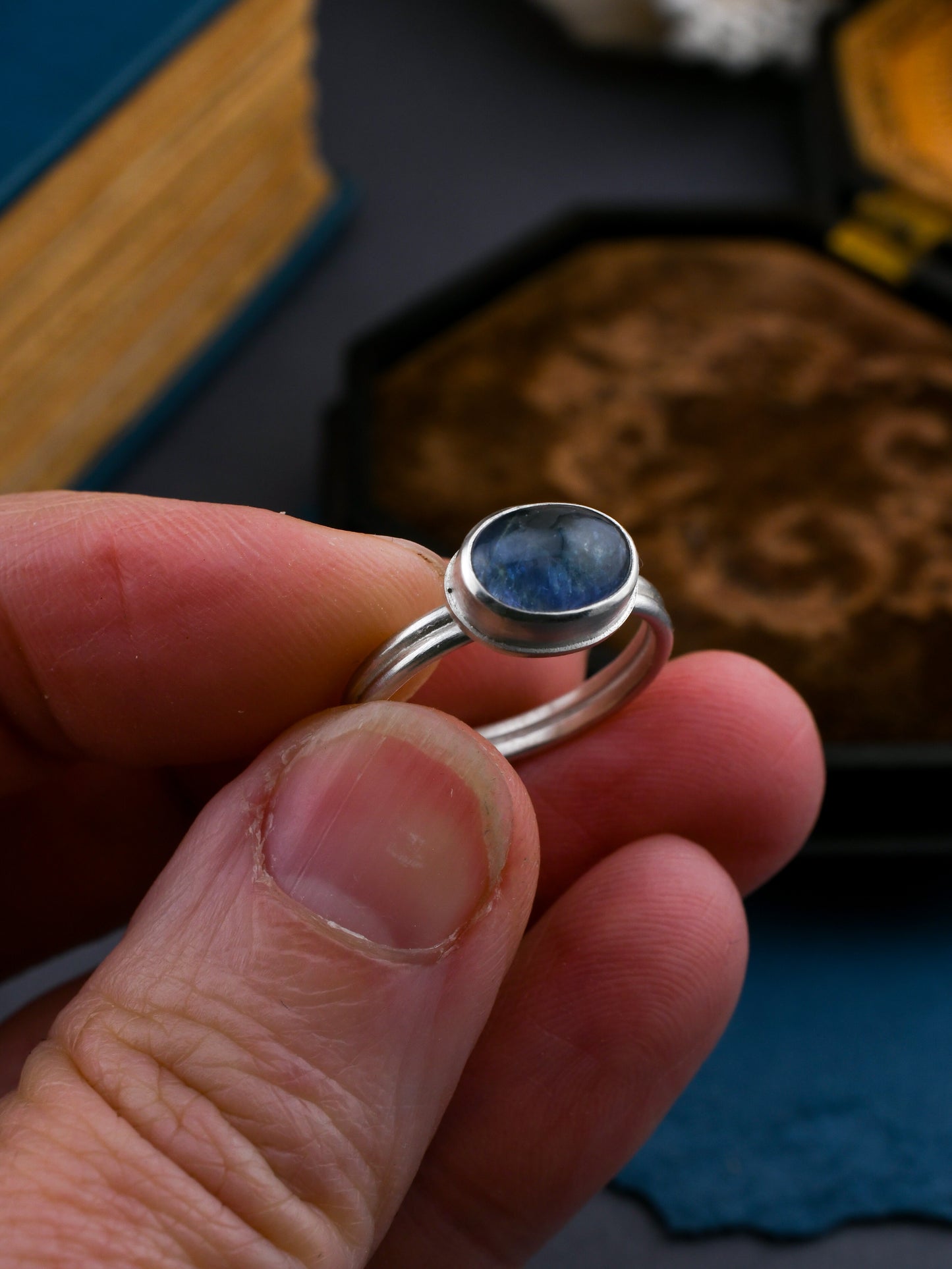 Silver ring with a blue stone held between fingers against a blurred background