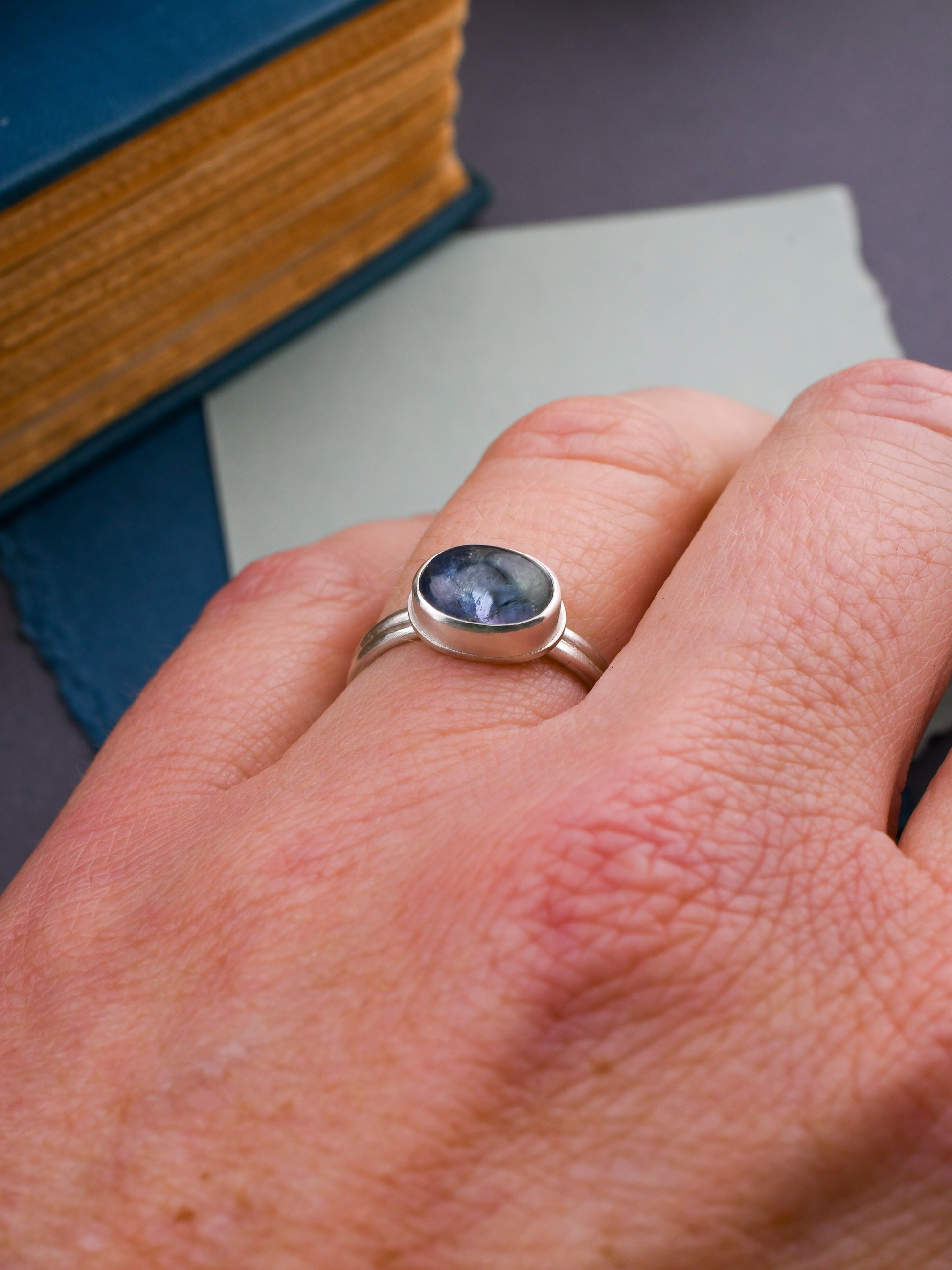 Hand wearing a silver ring with a blue gemstone, placed on books.