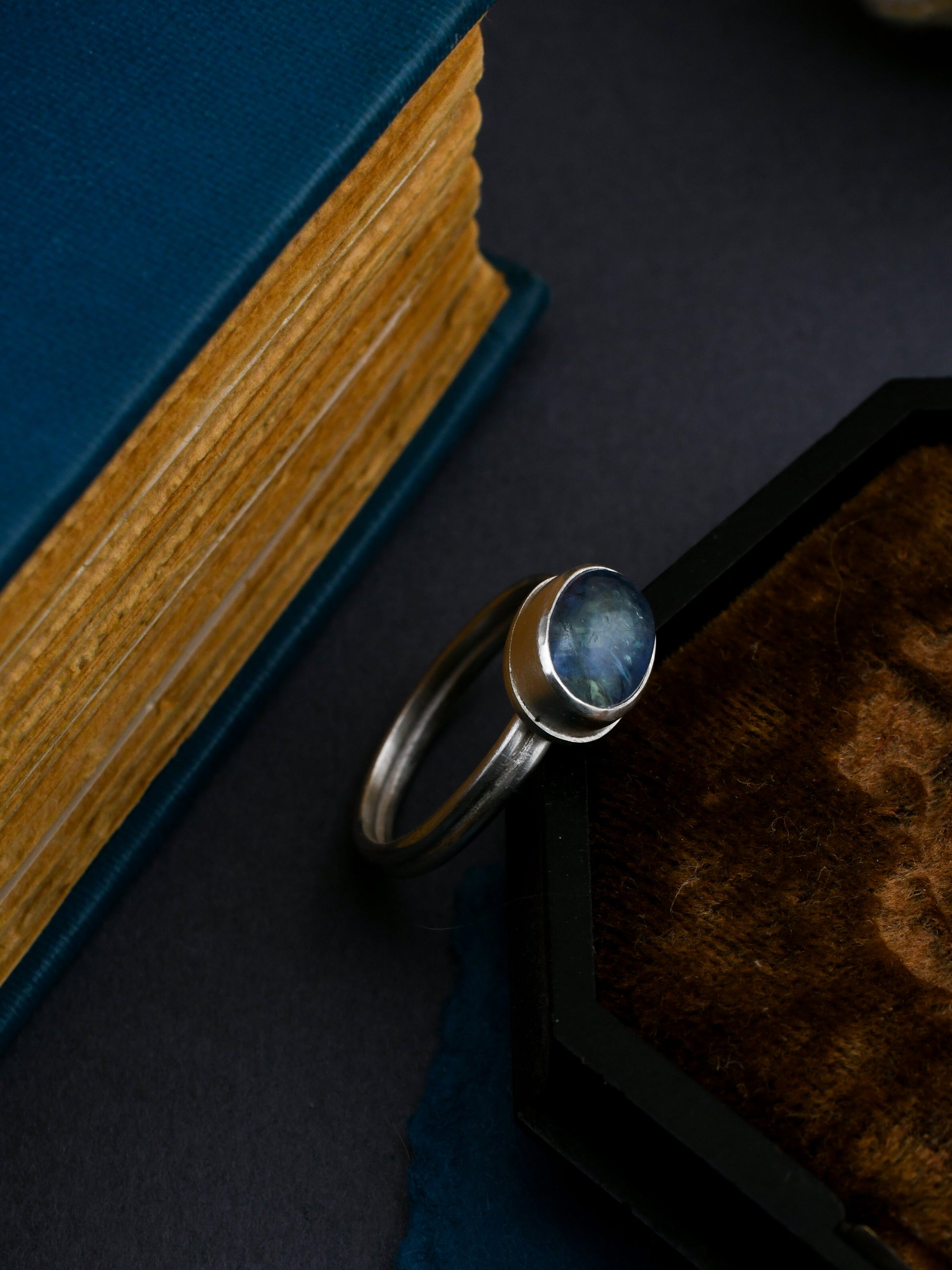 Silver ring with a blue stone on a dark surface next to a book